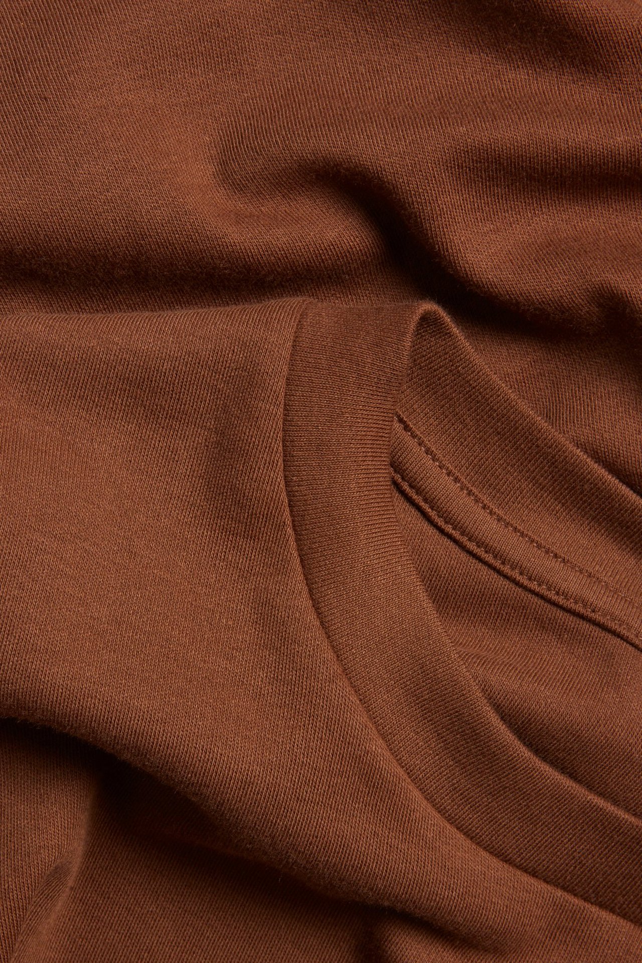 Zbliżenie brązowego, jednolitego, krótkiego bawełnianego T-shirtu, ukazujące teksturę materiału i szwy dekoltu.
