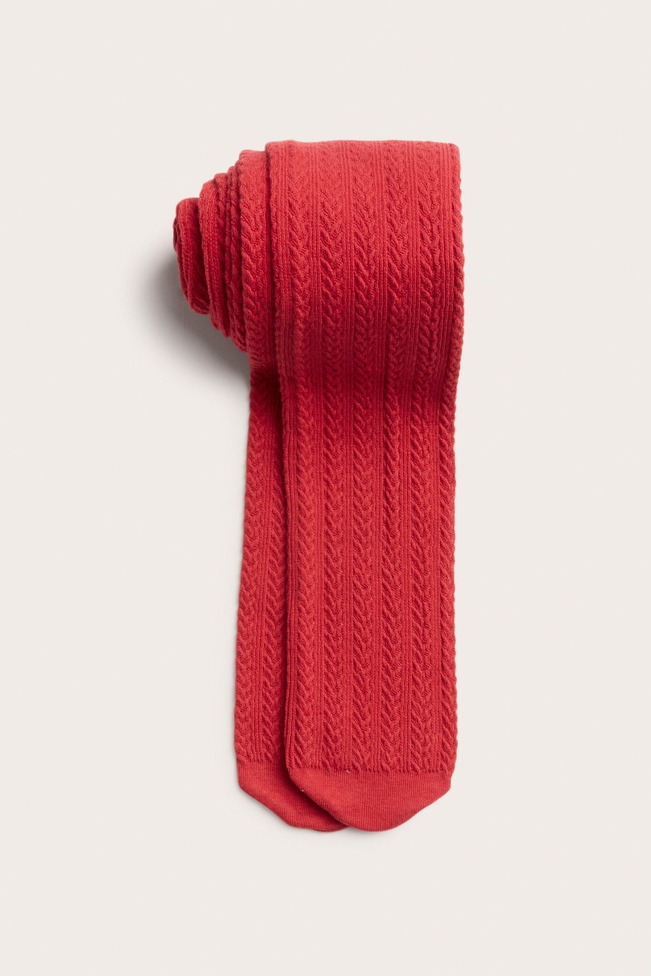 Lähikuva taitetuista punaisista palmikkoneulotuista puuvillasekoite sukkahousuista kuvioidulla pinnalla.