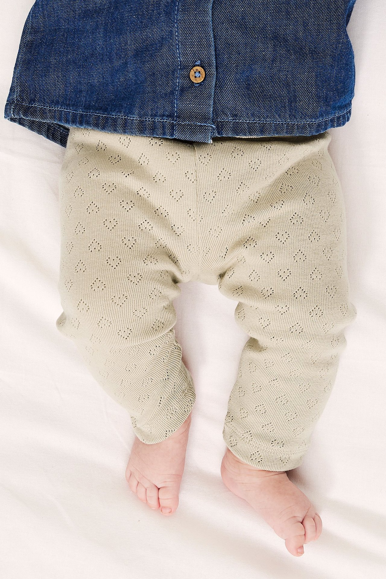 Widok z góry na dziecko w beżowych legginsach pointelle w serca i niebieskiej koszuli dżinsowej.