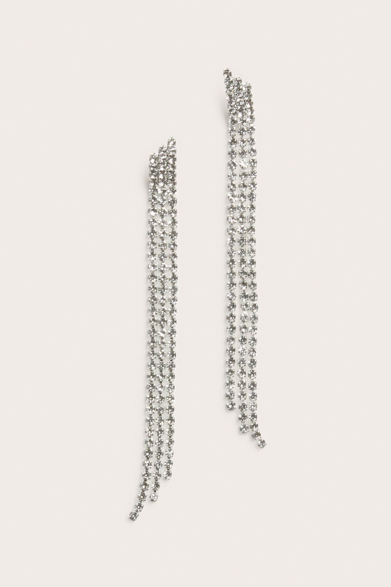 Zbliżenie dwóch długich, srebrnych kolczyków z cyrkoniami, każdy z trzema zwisającymi rzędami szklanych kamieni.