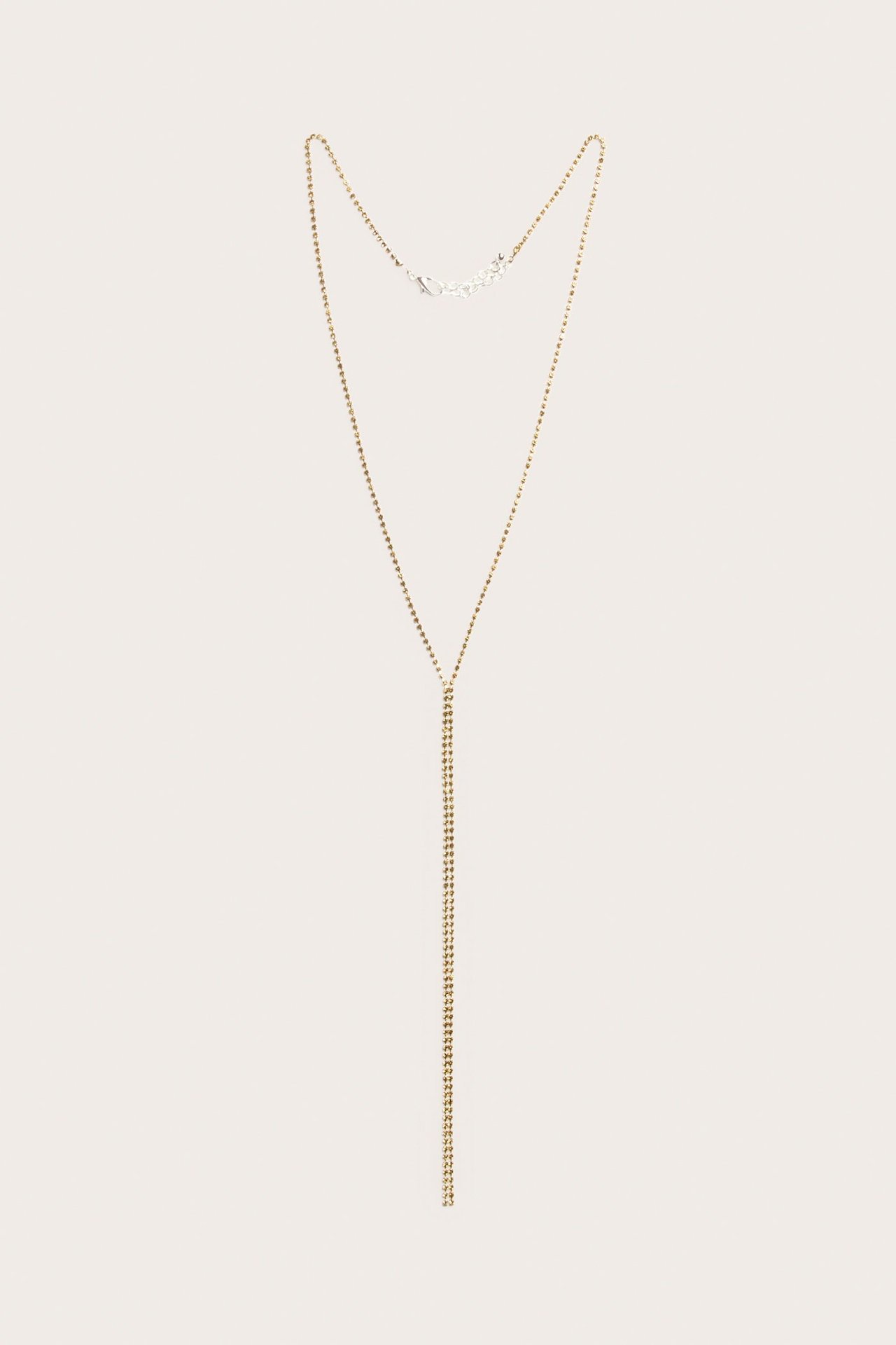 Edestä näkymä pitkästä, vaalean kullanvärisestä strass-lariat-kaulakorusta hopeanvärisellä papukaijalukolla.