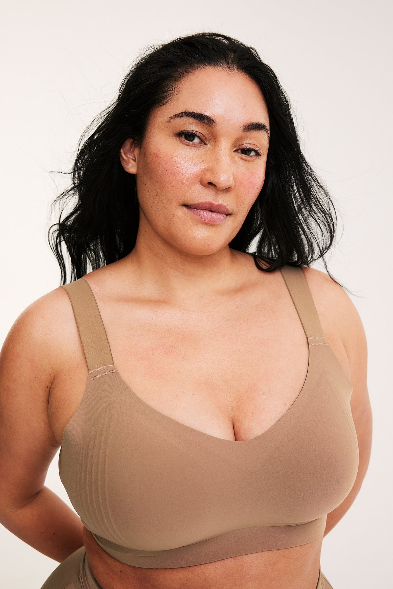 Zbliżenie z przodu: kobieta w jasnobrązowym, bezszwowym biustonoszu bez fiszbin, z szerokimi ramiączkami.