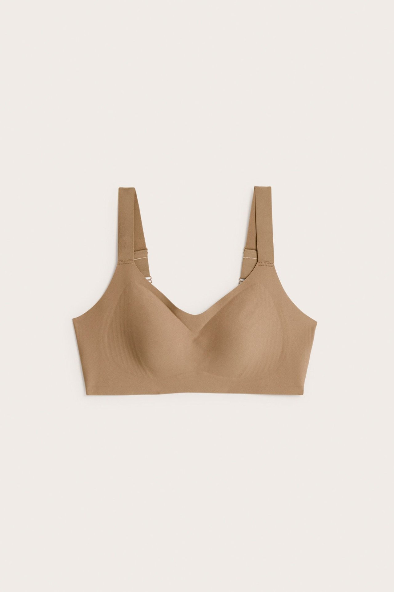 Frontvisning av en sømløs, beige trådløs dame-bh med brede justerbare stropper.