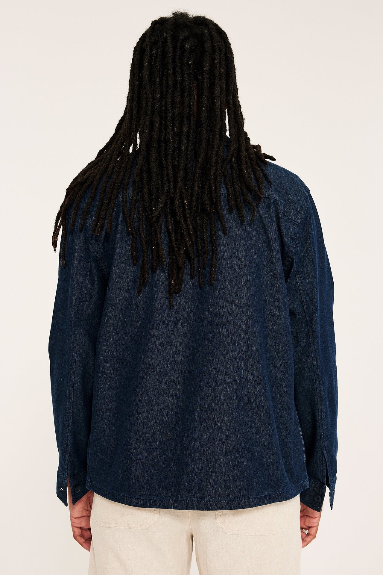 Ryggvy av man i en enfärgad mörkblå denim-overshirt och ljusbeige byxor.