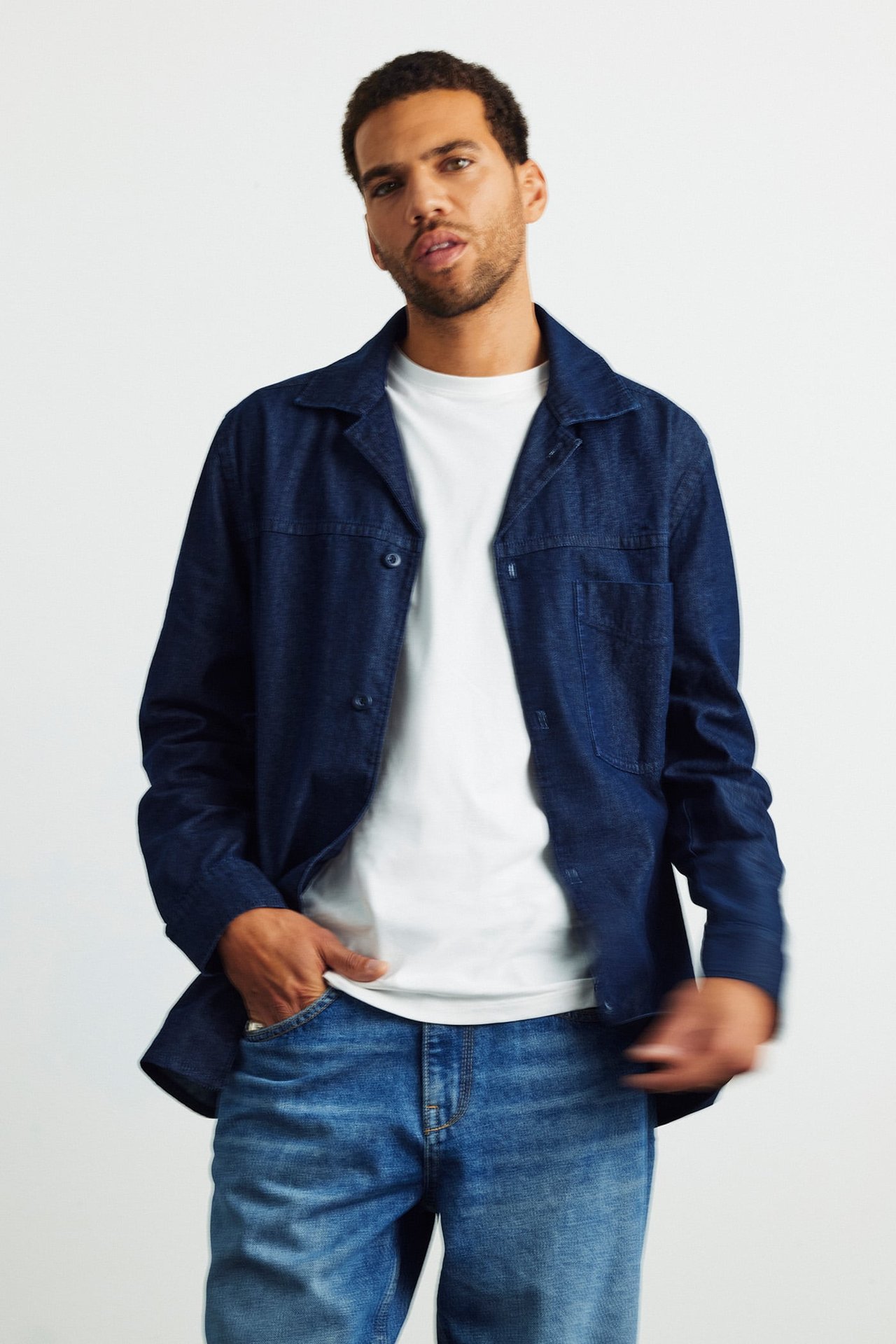 Edestä kuvattu mies tummansinisessä denim-overshirtissä, valkoisen t-paidan ja sinisten farkkujen kanssa.