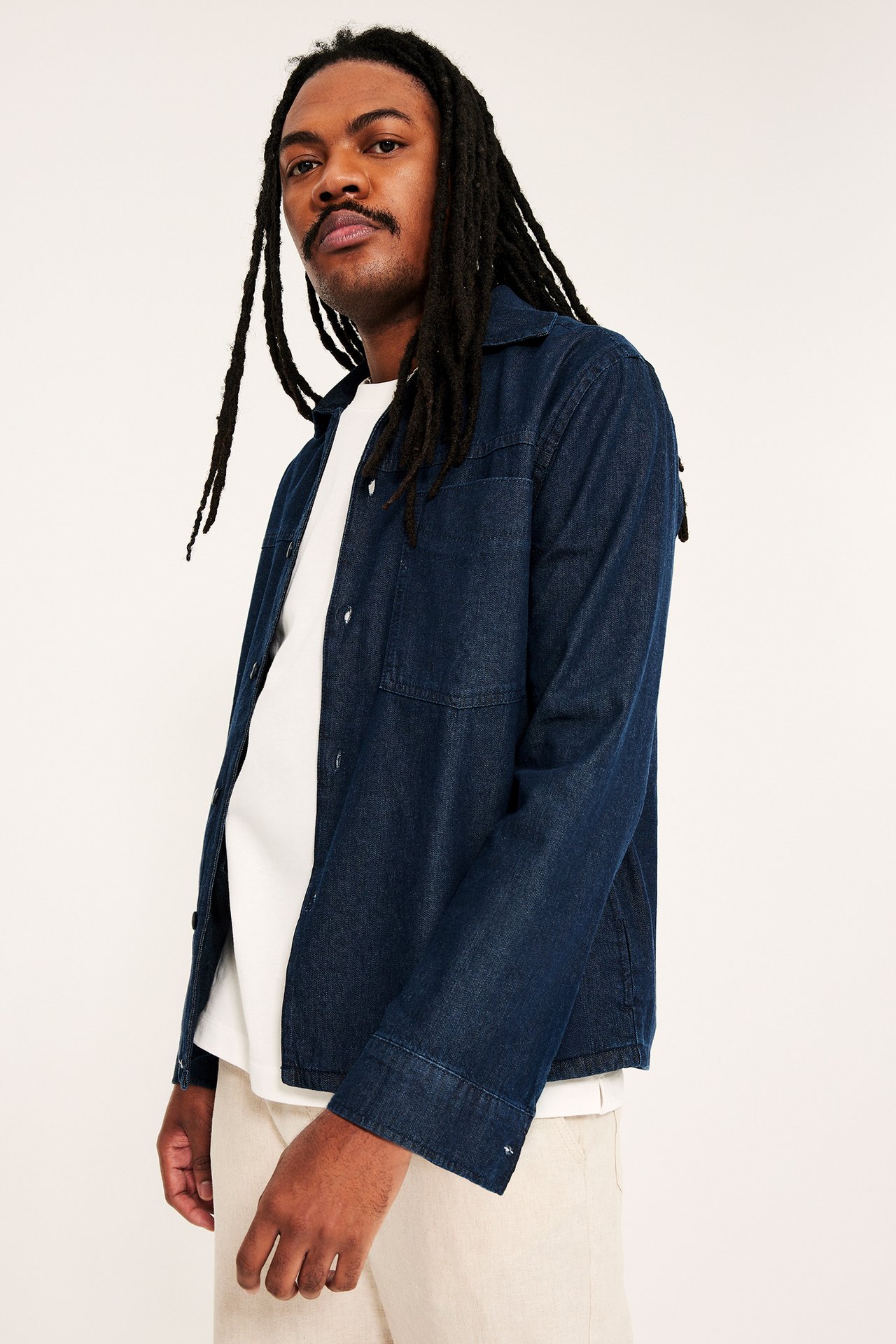 Sivukuva: mies tummansinisessä denim-overshirtissä valkoisen t-paidan ja vaaleabeigien housujen kanssa.