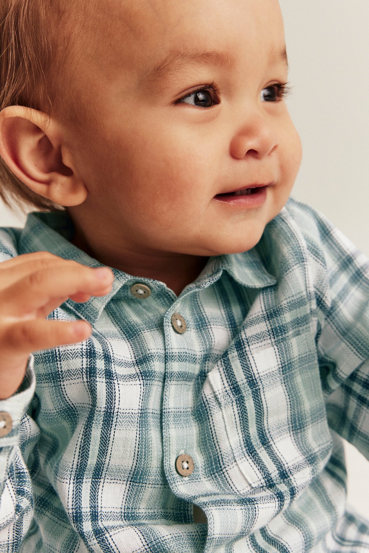 Nærbilde av baby i lys grønn rutete bomulls skjortebody med knapper.