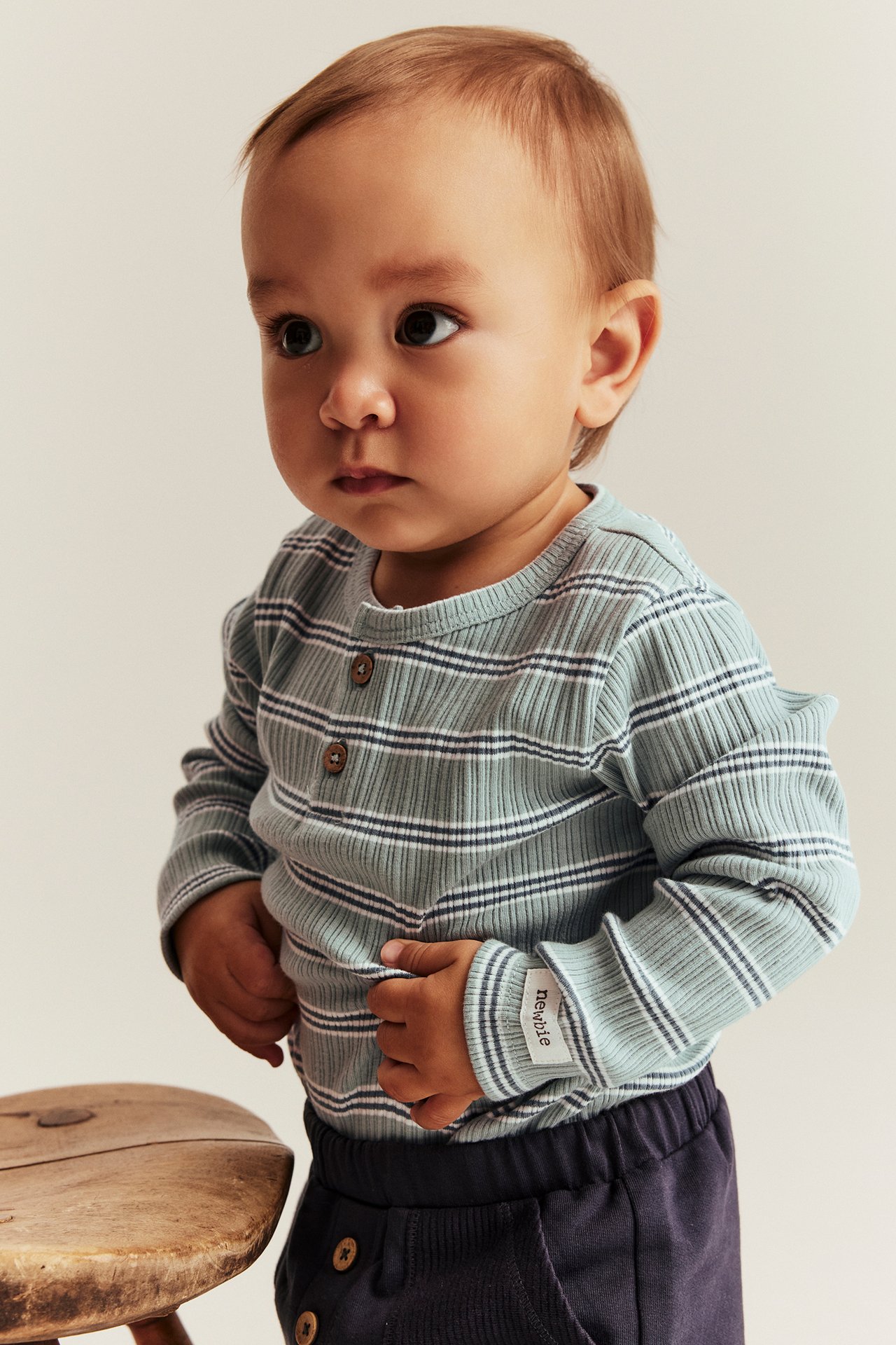 Edestä, vauva yllään vaaleanvihreä raidallinen ribbineulebody kahdella napilla, yhdistettynä tummansinisiin housuihin.