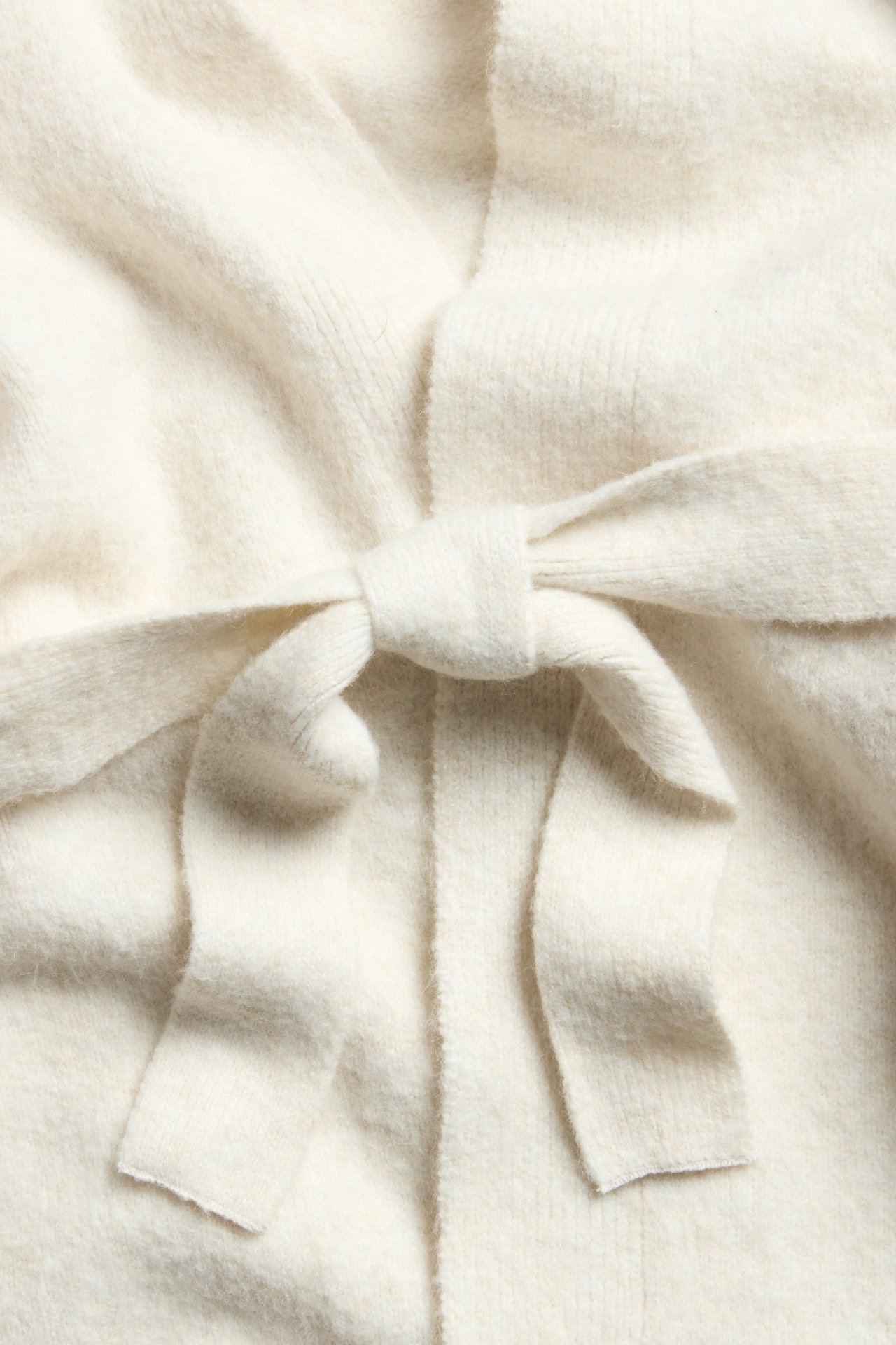 Lähikuva valkoisesta meleeratusta neuleneuletakista, jossa on solmittu vyötärönauha edessä.