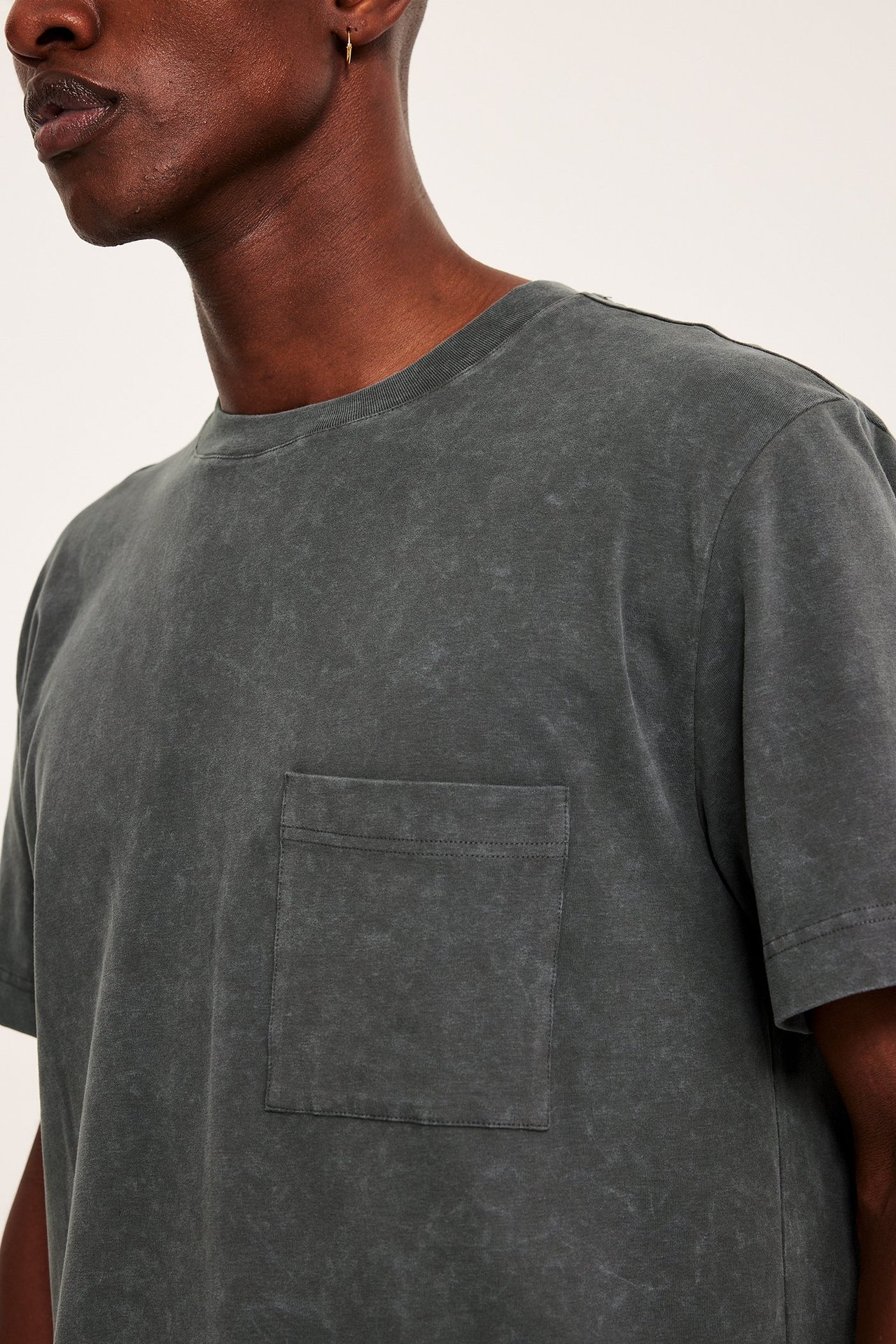 Framifrån, man i en mörkgrå tvättad t-shirt med rund hals och bröstficka.