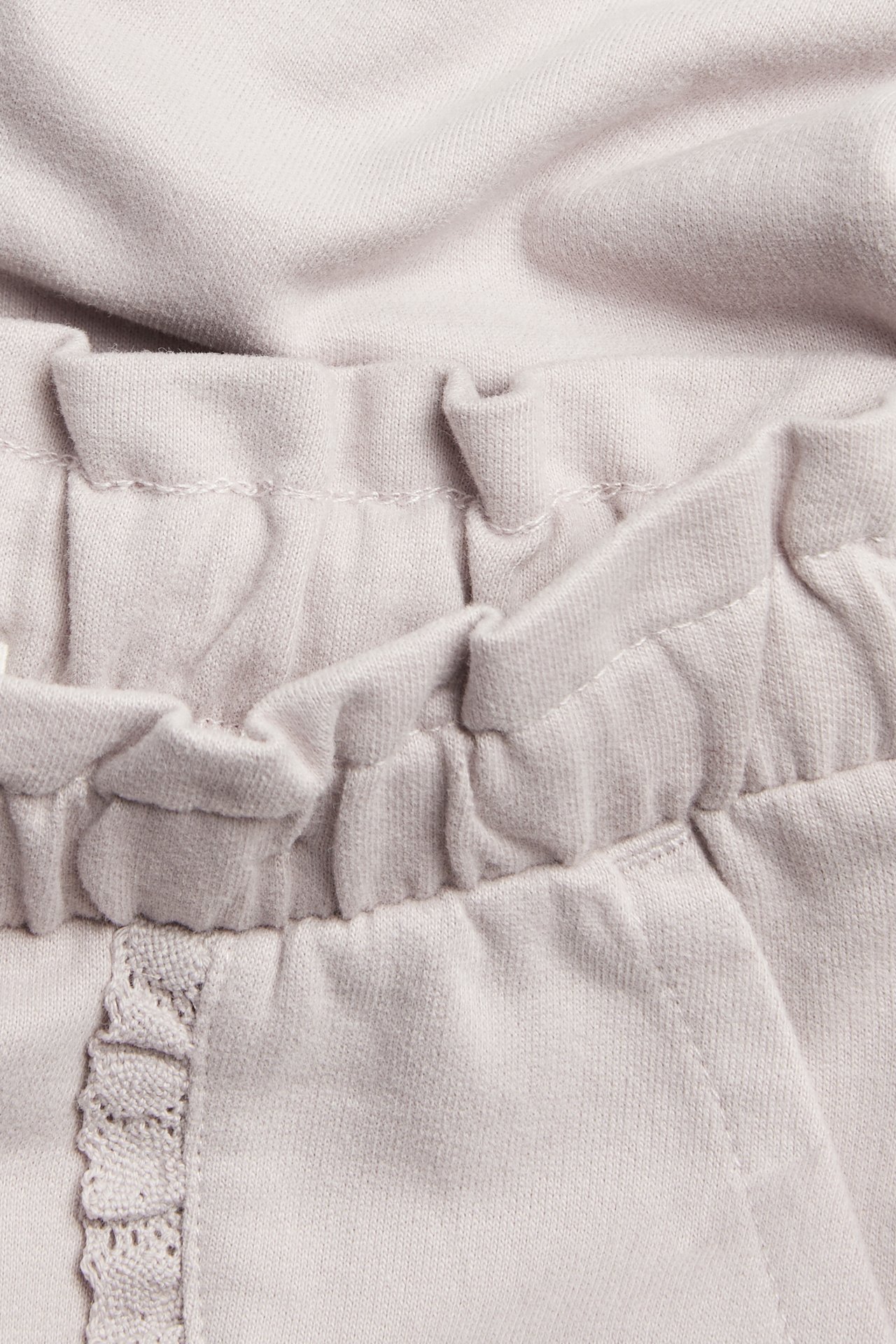 Zbliżenie dziecięcych jasnofioletowych bawełnianych spodni dresowych z elastycznym pasem i koronkową kieszenią.