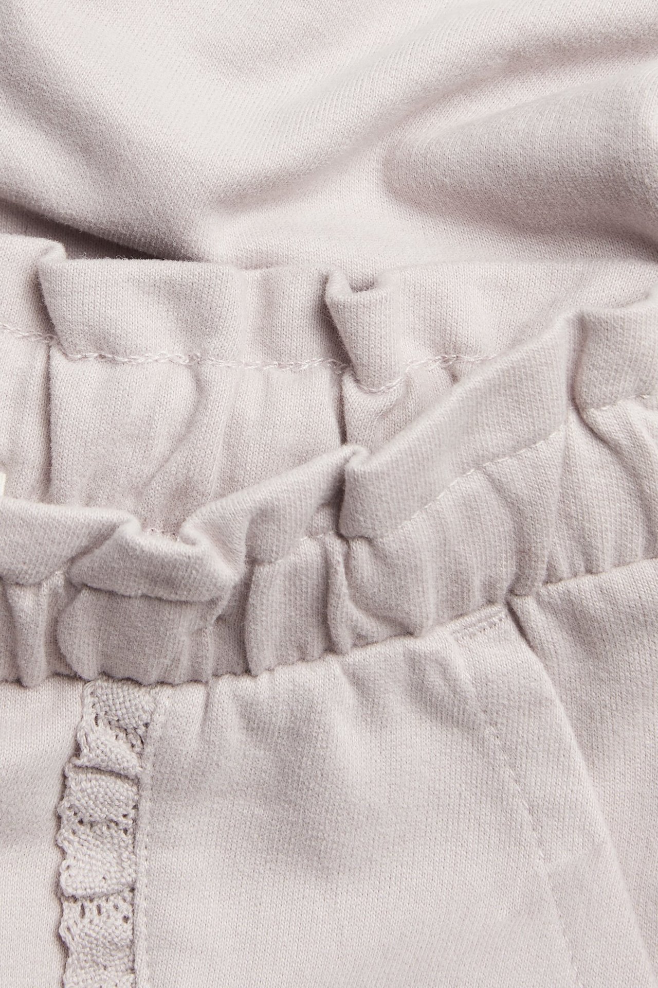 Nærbilde av barnas lyslilla bomulls-joggebukse med elastisk linning og blondekantet lomme.