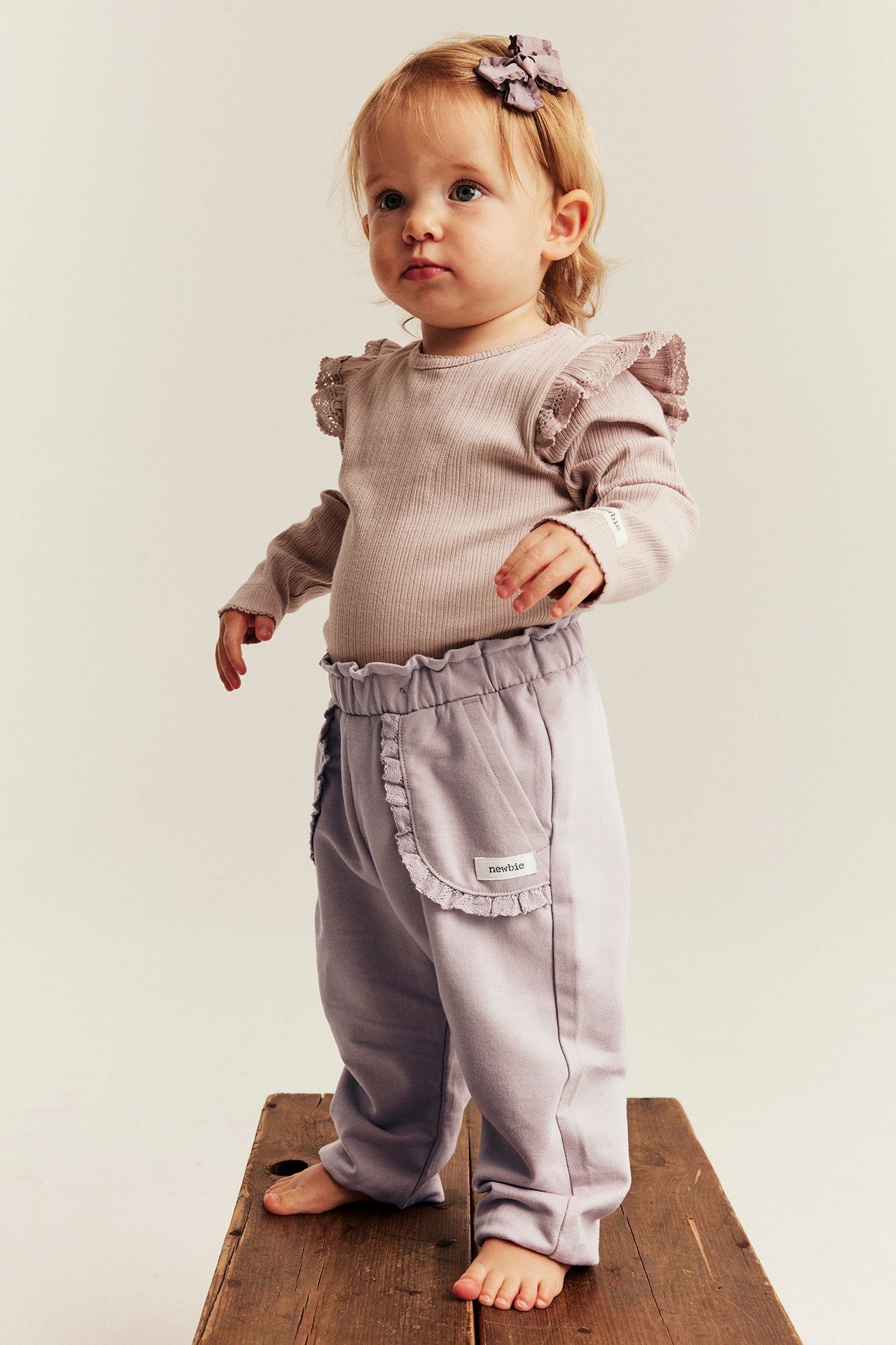 Front, baby i lys lilla volangbukse, ribbet body og lilla hårsløyfe.
