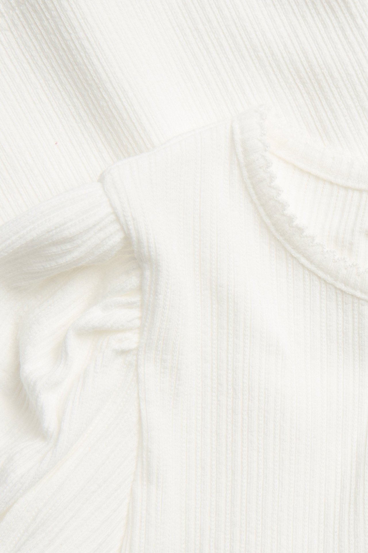 Zbliżenie na kremowy prążkowany top z krótkimi bufiastymi rękawami i obszyciem pikot.