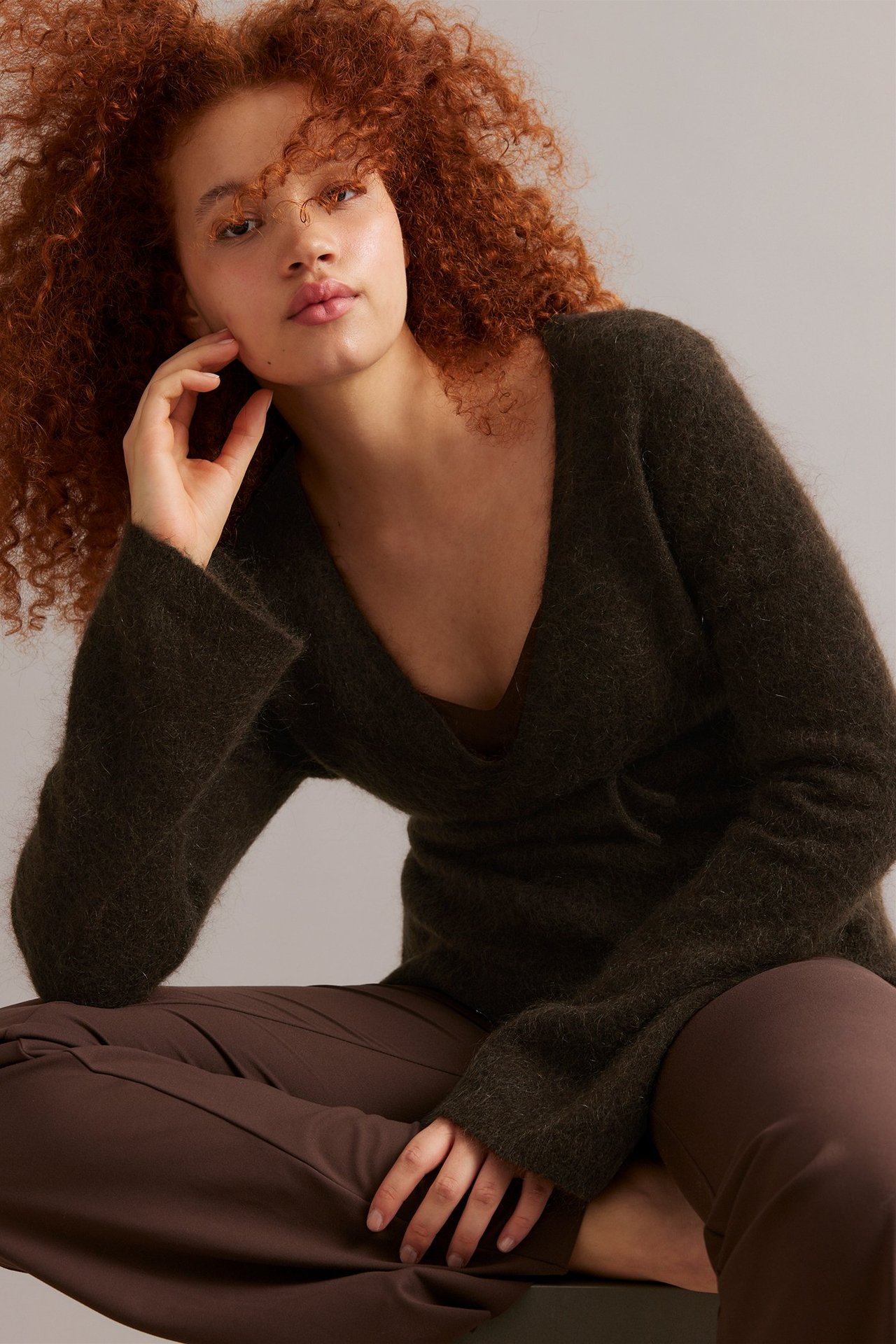 Edestäpäin: nainen tummanruskeassa villasekoite kietaisuneuletakissa ja ruskeissa housuissa.