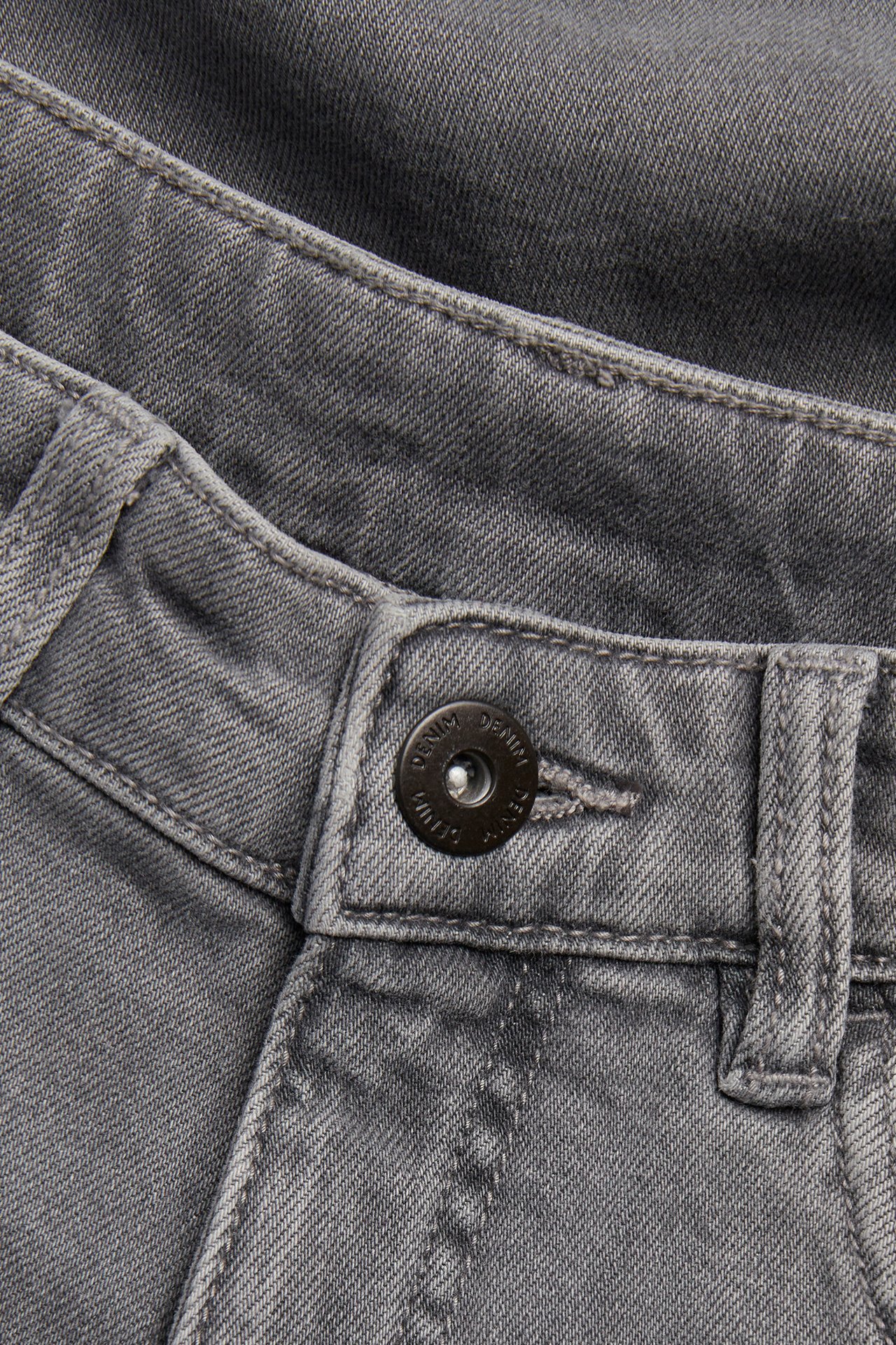 Zbliżenie jasnoszarych luźnych jeansów ze średnim stanem i czarnym zapięciem na guzik.