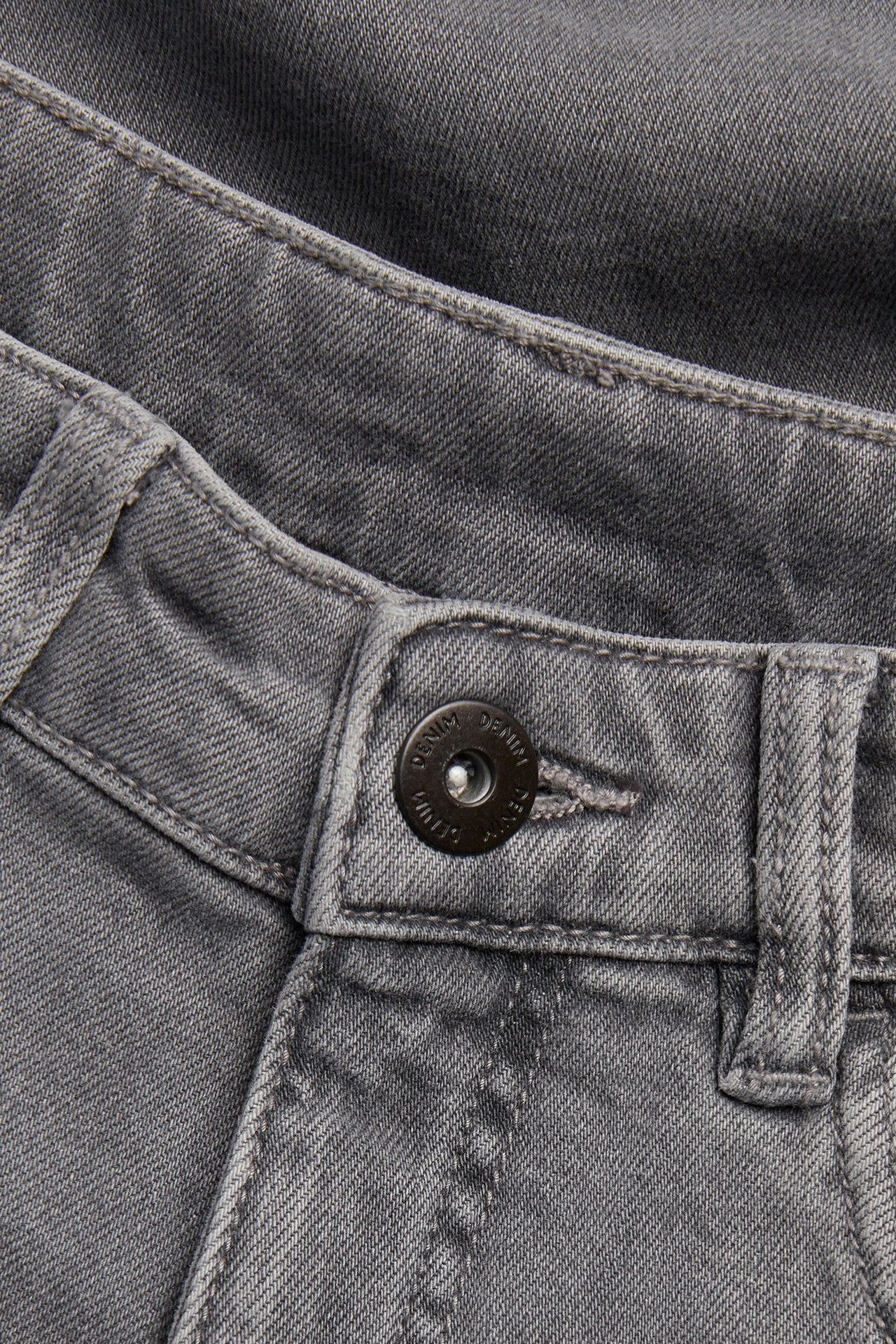 Zbliżenie jasnoszarych luźnych jeansów ze średnim stanem i czarnym zapięciem na guzik.