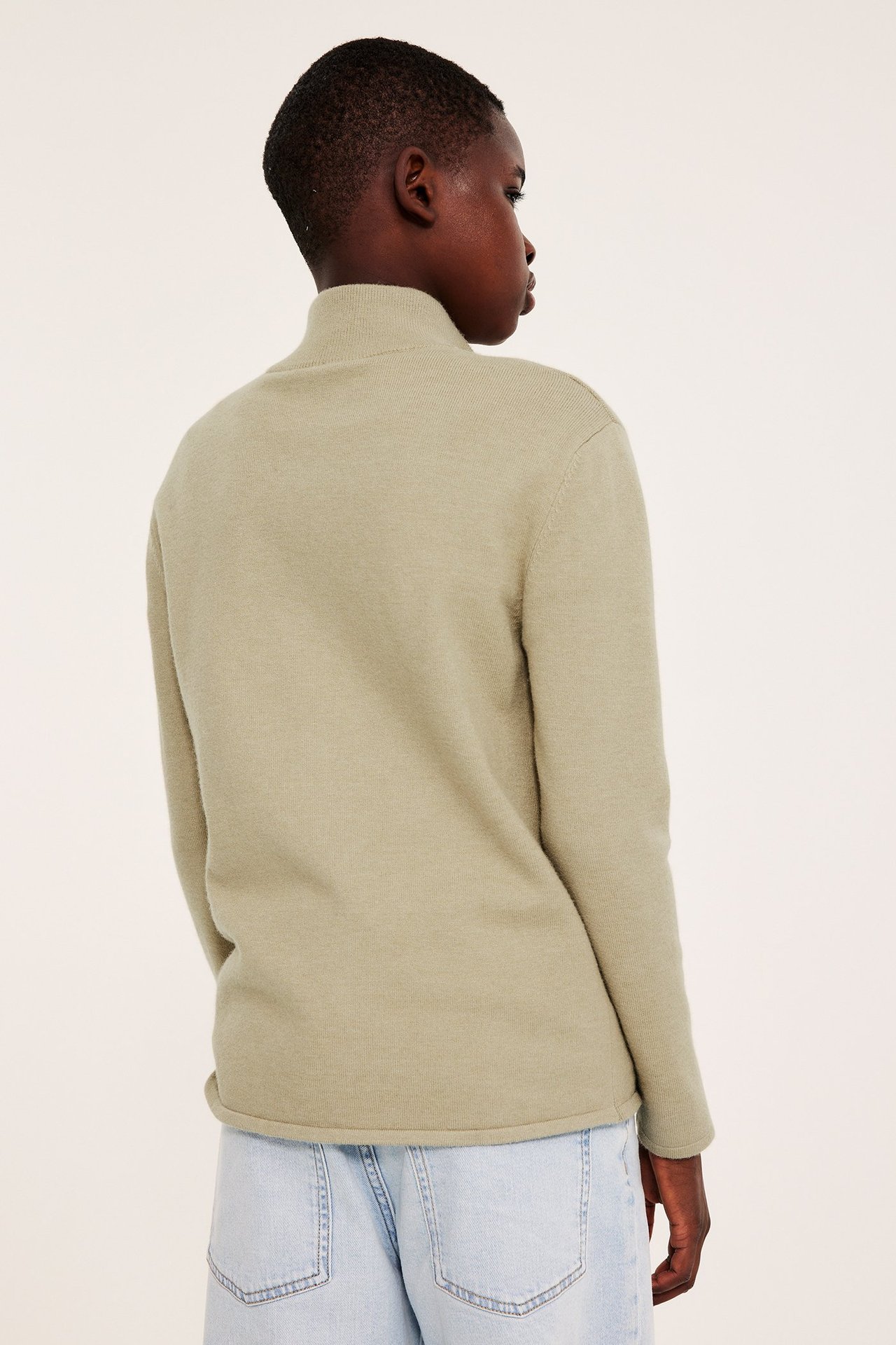 Lasten beige meleerattu neulepusero korkealla kauluksella, yllään vaaleansiniset farkut, takaapäin.