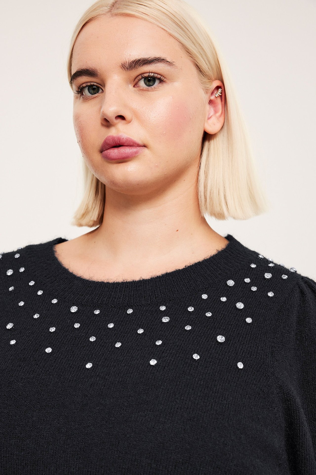 Zbliżenie na kobietę w czarnym dzianinowym swetrze z dżetami, z srebrnym liściastym nausznikiem.