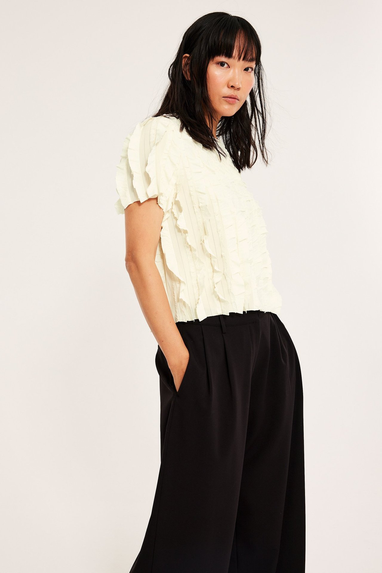 Kobieta w białym topie z falbankami i czarnych szerokich spodniach.