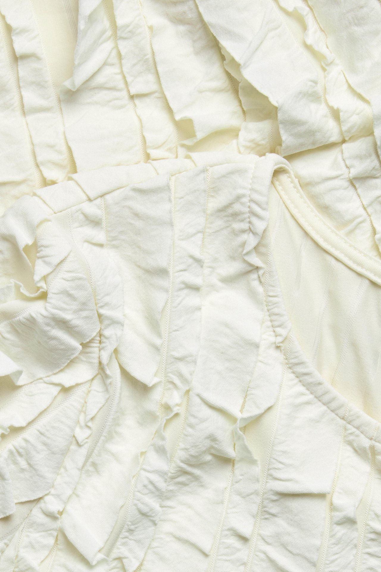 Zbliżenie na kremowy, strukturalny top z licznymi falbanami, wykonany z mieszanki poliestru.