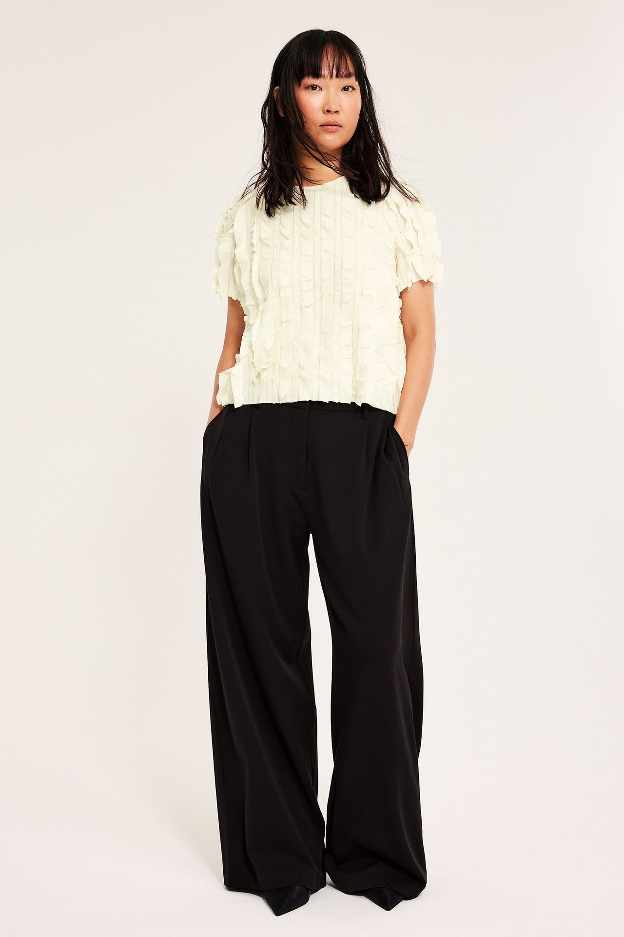 Kobieta ubrana w kremową top boxy z falbankami, na czarne spodnie.