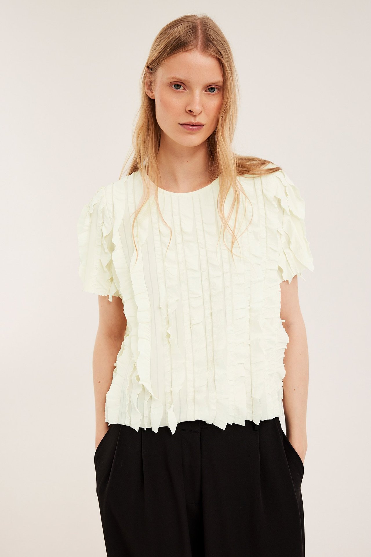 Widok z przodu: kobieta w ecru topie z falbanami i krótkimi rękawami, czarne spodnie.