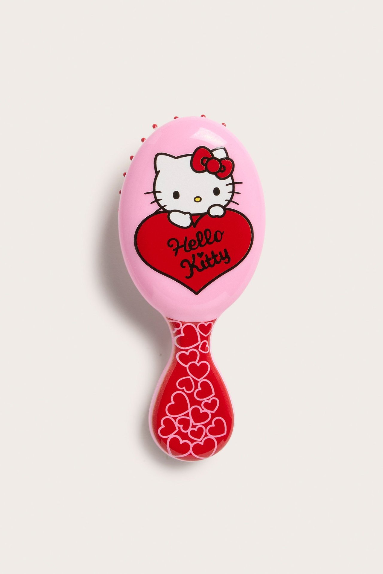 Forfra rosa Hello Kitty hårbørste med rødt hjerte og mønstret rødt håndtak.