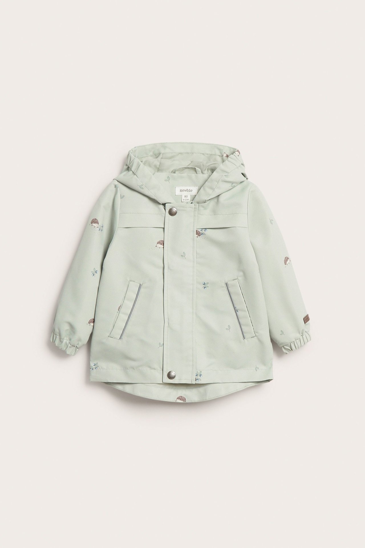 Edestäpäin kuvattu lasten vaaleanvihreä hupullinen takki siilikuviolla, vetoketjulla ja nepparikiinnityksellä.