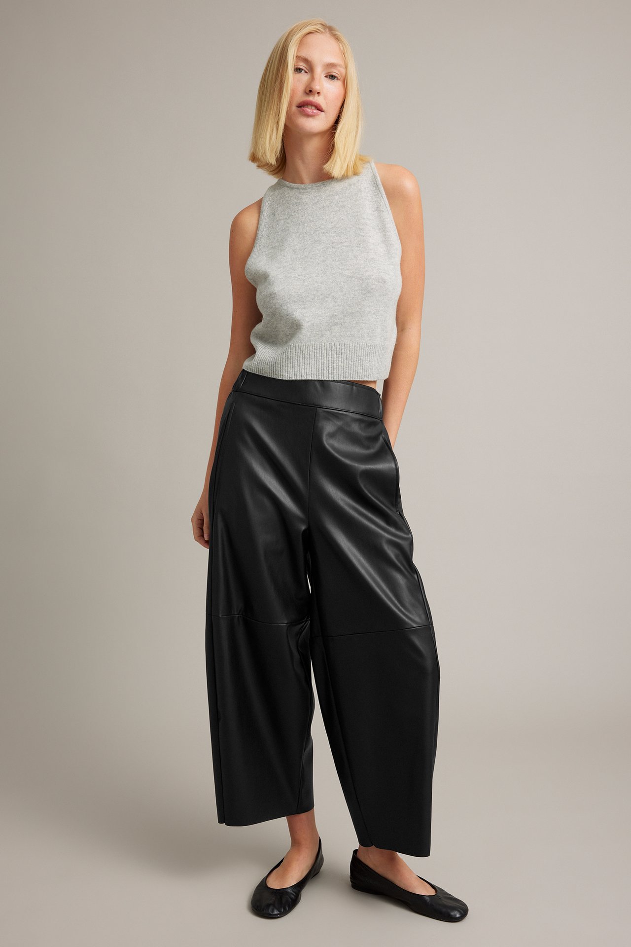 Kvinna i svarta culottes i fuskläder, grå stickad topp och svarta ballerinaskor.