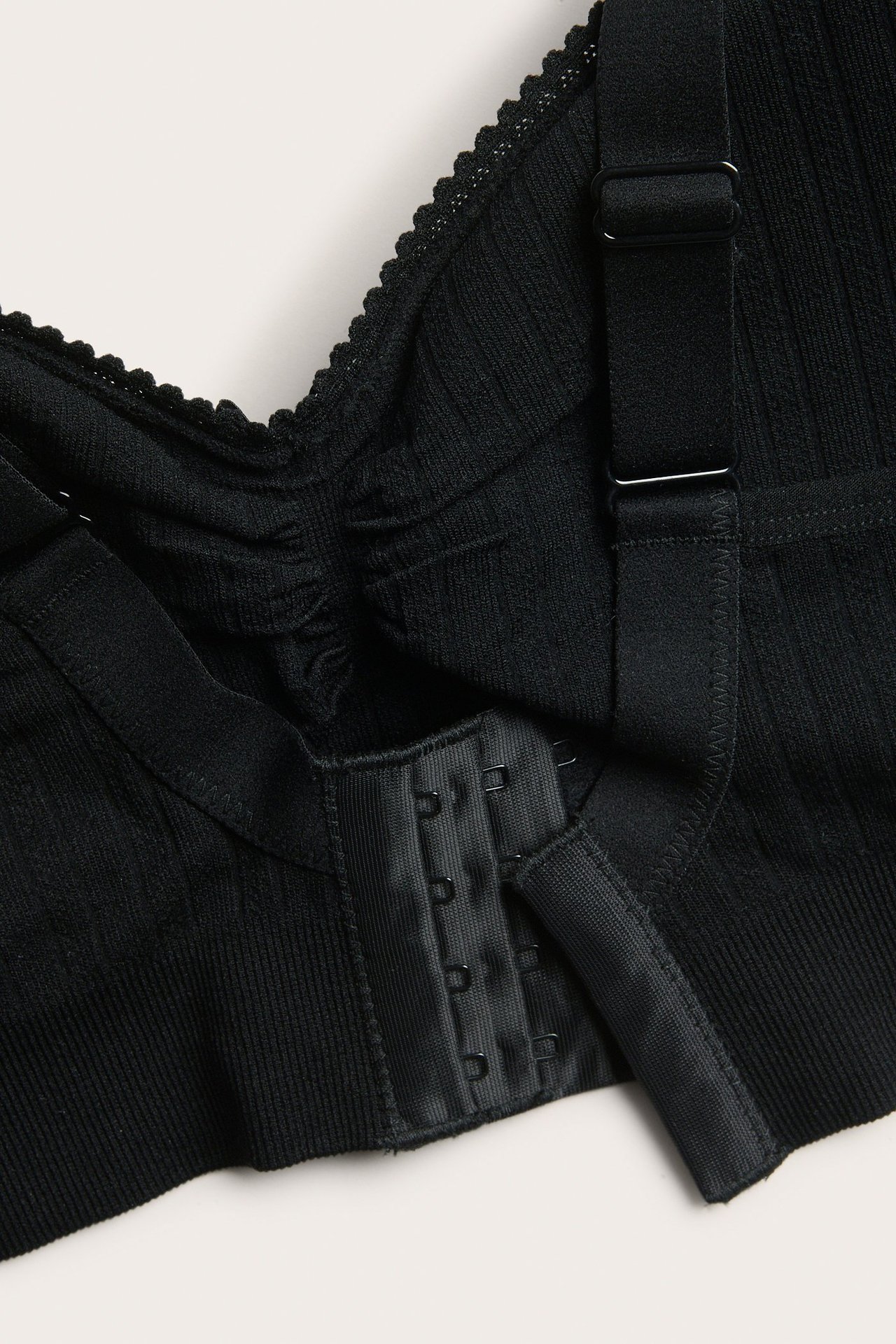 Zbliżenie na czarny biustonosz bezszwowy, prążkowany, z czterorzędowym zapięciem na haftki i regulowanym ramiączkiem.