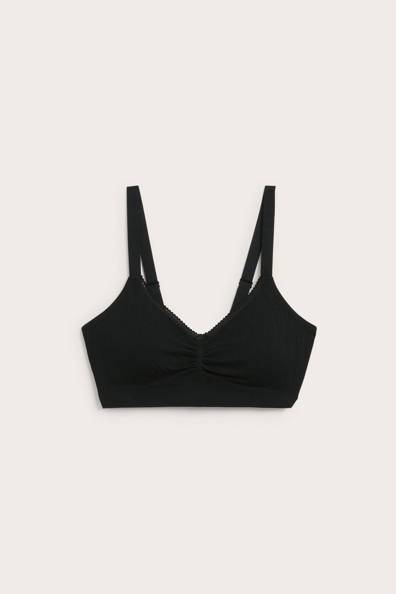 Edestäpäin, musta saumaton rintaliivi pointelle-kuviolla, picot-reunaisilla olkaimilla ja pienellä rusetilla.