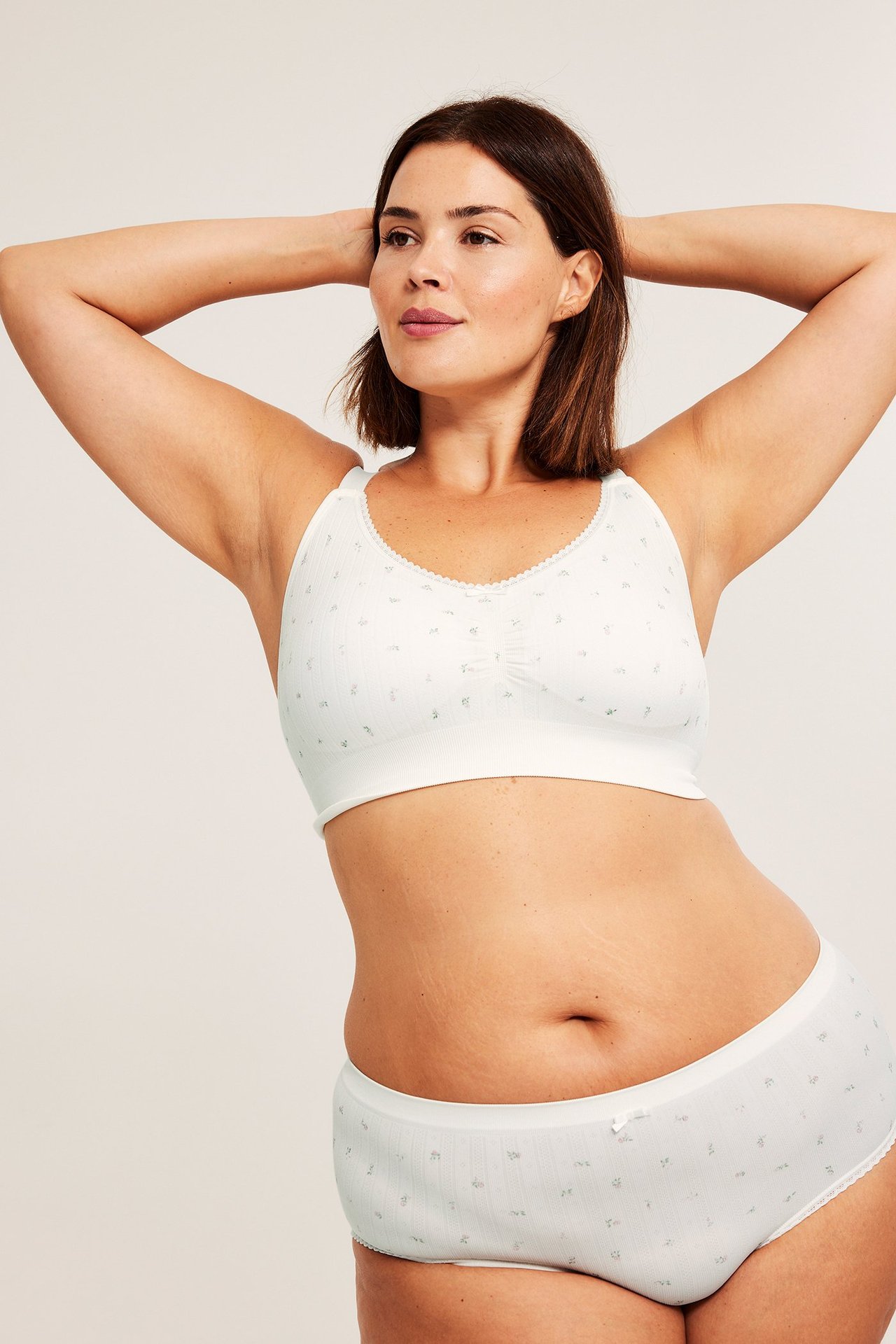 Widok z przodu kobiety w kremowym kwiecistym bezszwowym biustonoszu z wykończeniem picot i pasującymi majtkami.