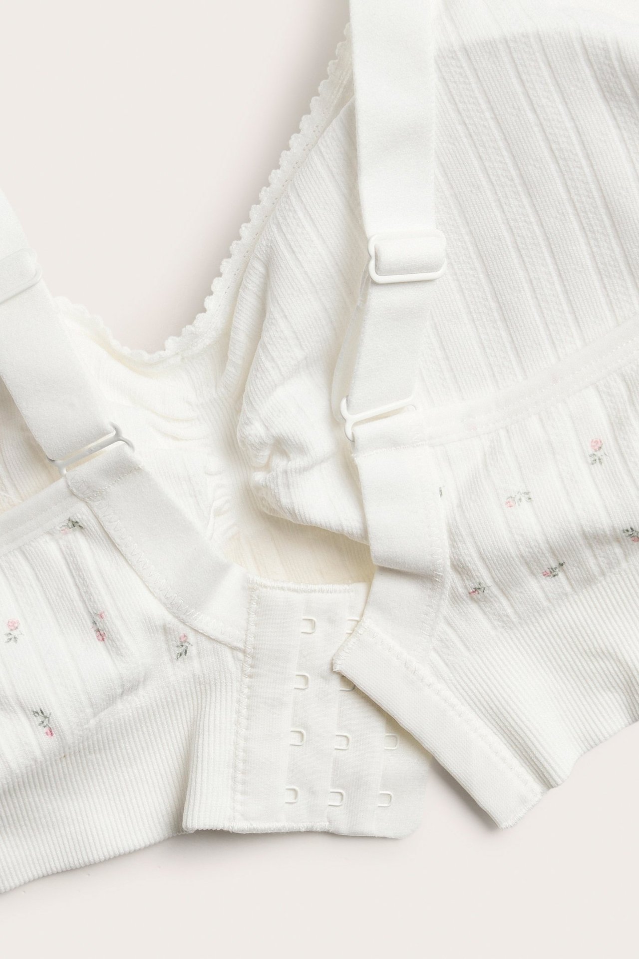 Zbliżenie: Biały bezszwowy biustonosz z drobnym różowym kwiatowym wzorem, prążkowana tkanina, regulowane ramiączka, czterorzędowe zapięcie.