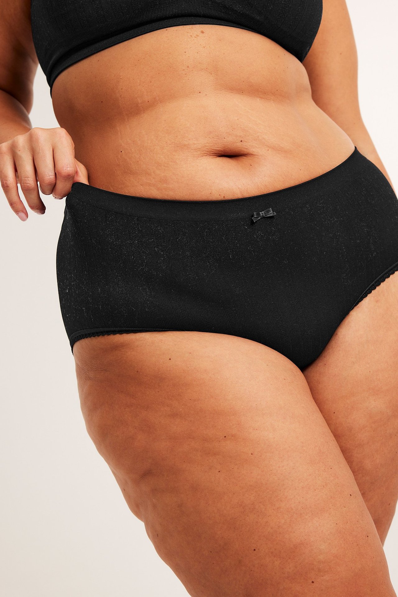 Zbliżenie z przodu kobiety w czarnych bezszwowych figach hipster z kokardką i czarnym topie biustonoszowym.