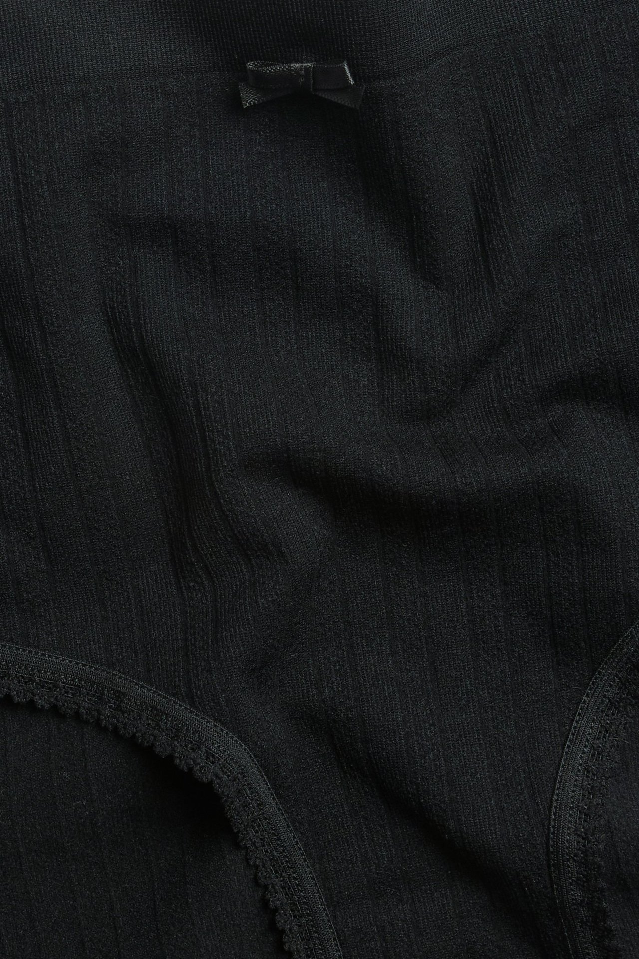 Widok z przodu czarnych bezszwowych fig typu hipster z teksturą pointelle, małą kokardką i obszyciem picot.