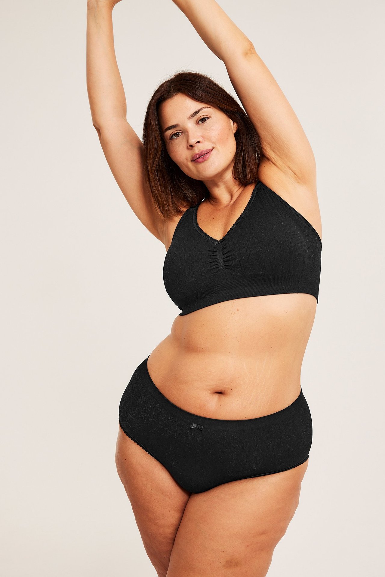 Frontbilde av en kvinne i svart sømløs pointelle hipster truse med sløyfe og matchende BH.
