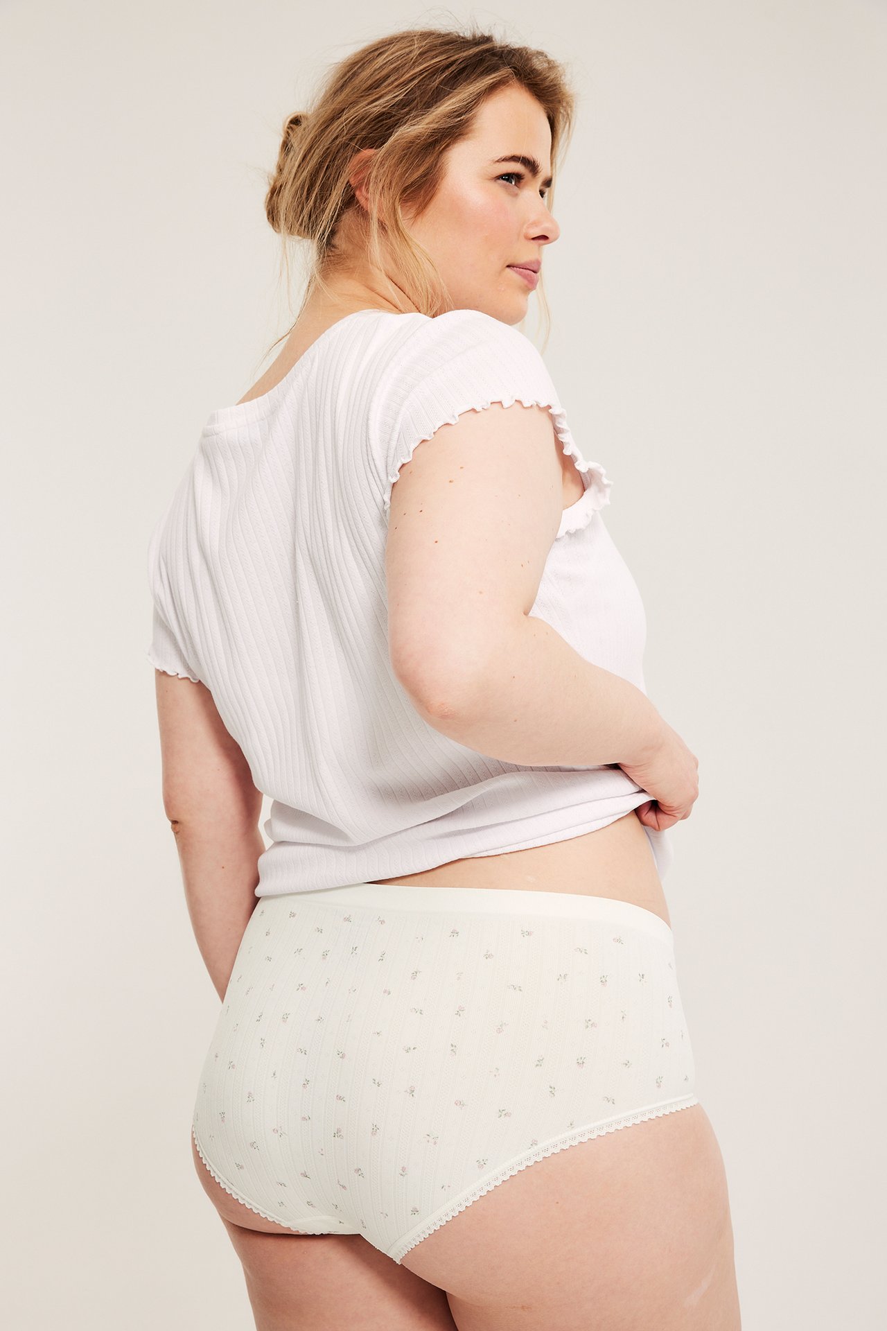 Naisen takakuva, yllään luonnonvalkoiset kukkakuvioiset hipsterit ja valkoinen ribbipaita.