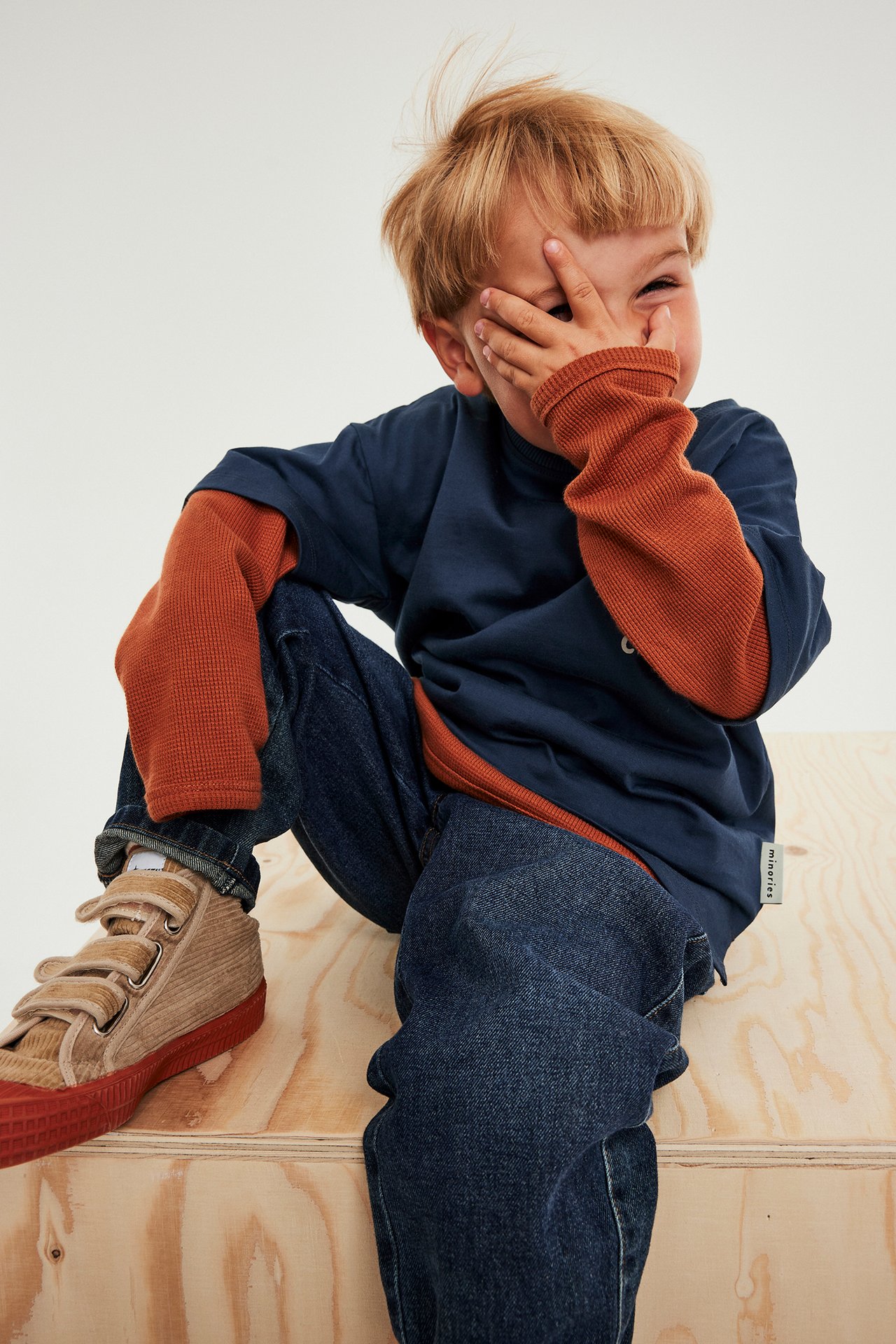 Barn manlig modell i mörkblå t-shirt med djurmönster, orange långa ärmar, jeans och sneakers.