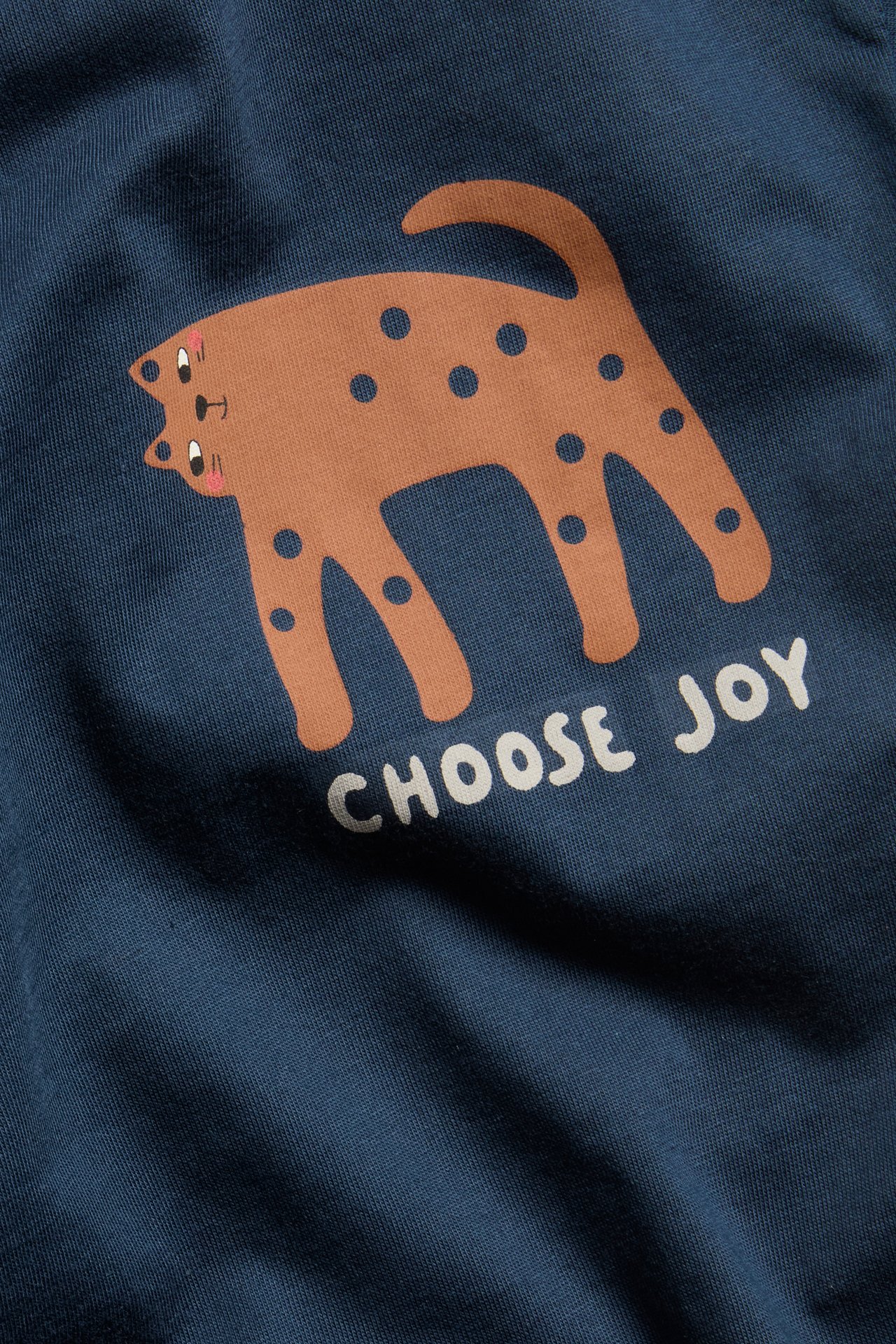 Kortärmad t-shirt med tryck av en djurmönstrad katt i brun och blått, text 'CHOOSE JOY'.