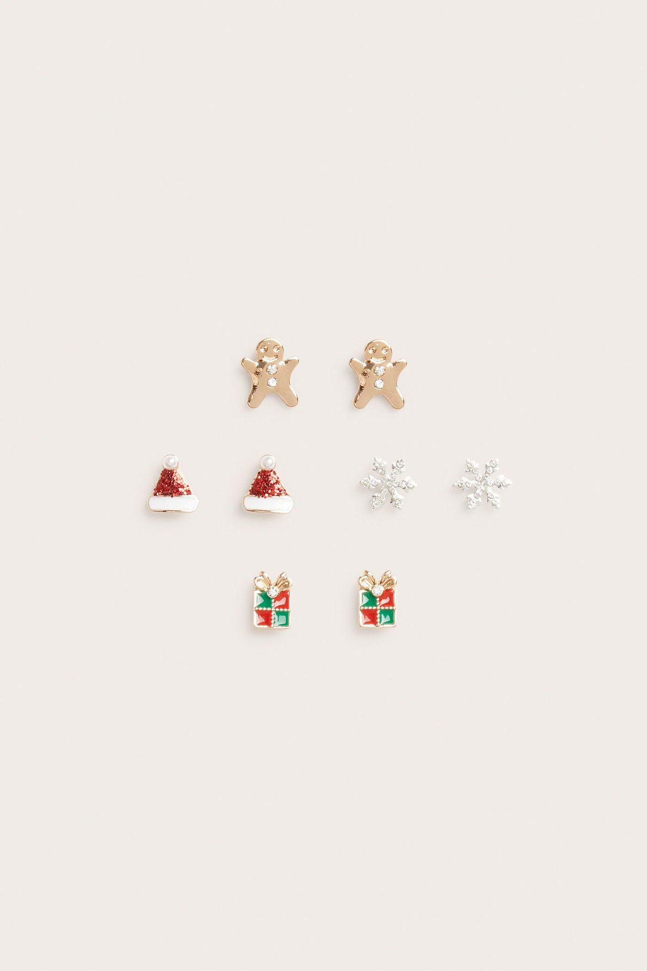 Lähikuva neljästä joulukorvakoruparista: kultaiset piparkakkuihmiset, punaiset tonttulakit, hopeiset lumihiutaleet, punavihreät lahjat.