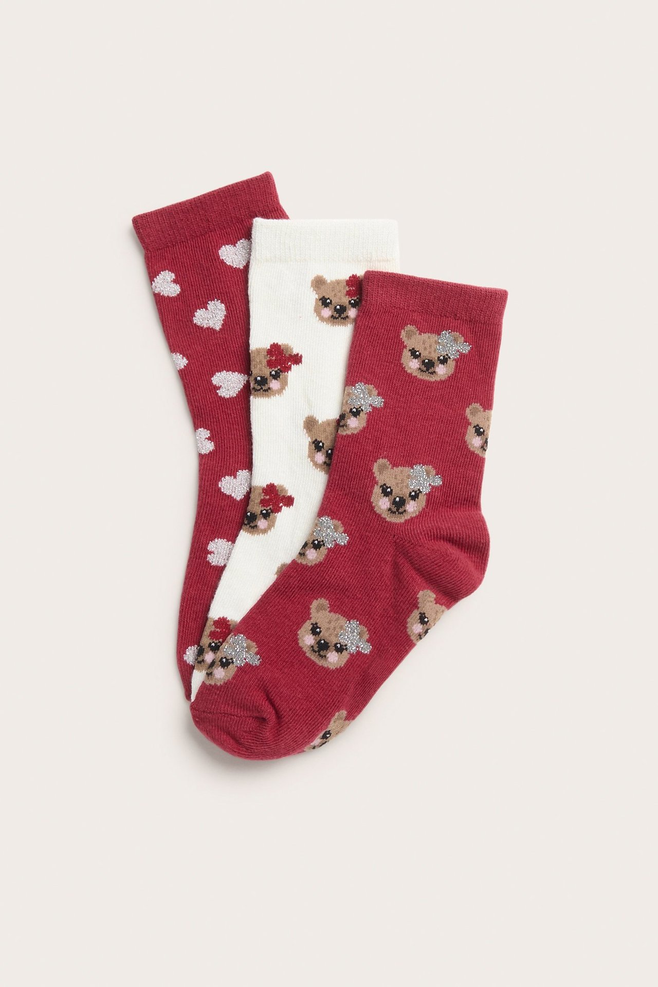 Zbliżenie: Trzy wzorzyste skarpetki dziecięce. Czerwone w serca, ecru w misie, czerwone w misie.