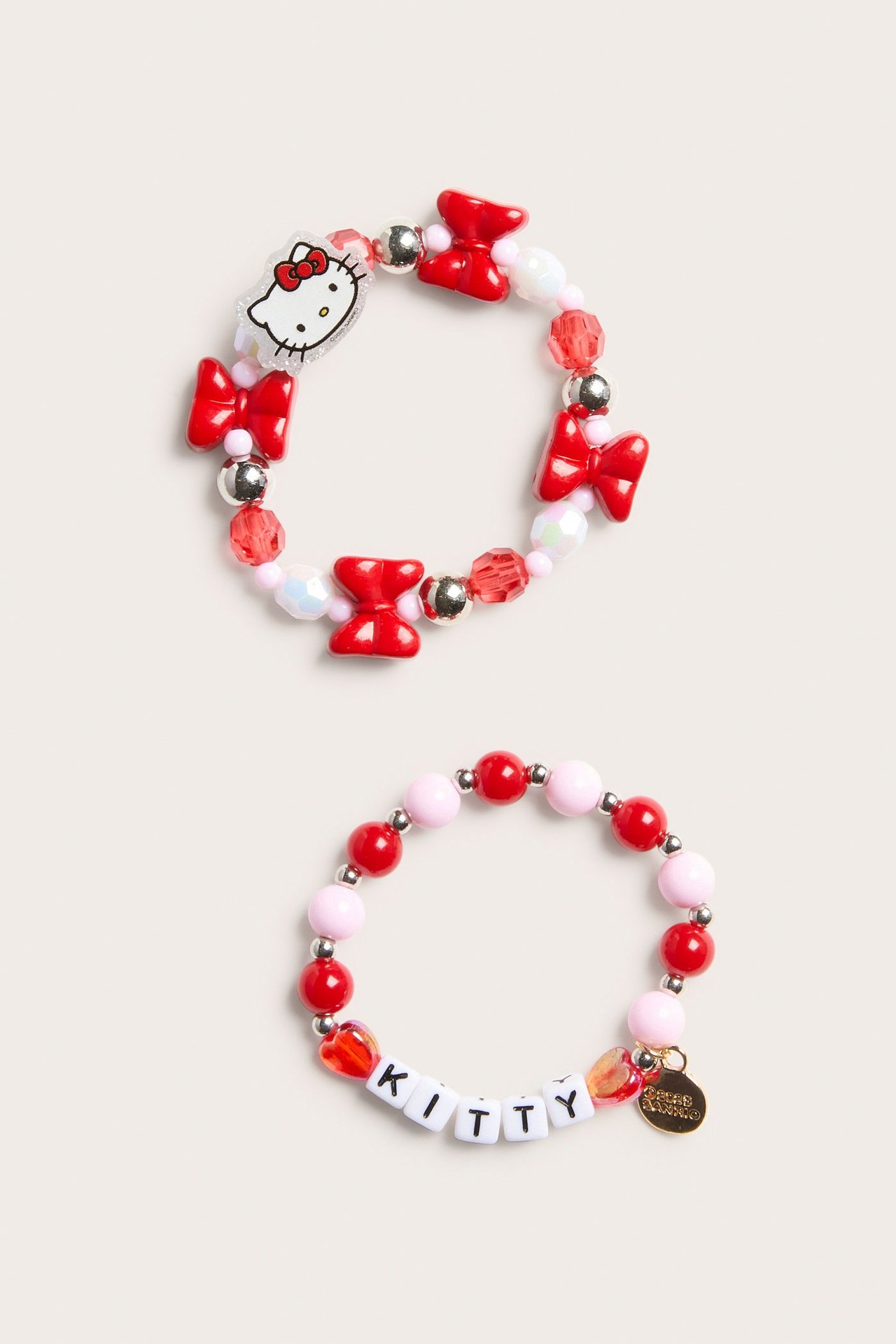 Zbliżenie na dwie różowo-czerwone bransoletki Hello Kitty; jedna z zawieszką i czerwonymi kokardkami.