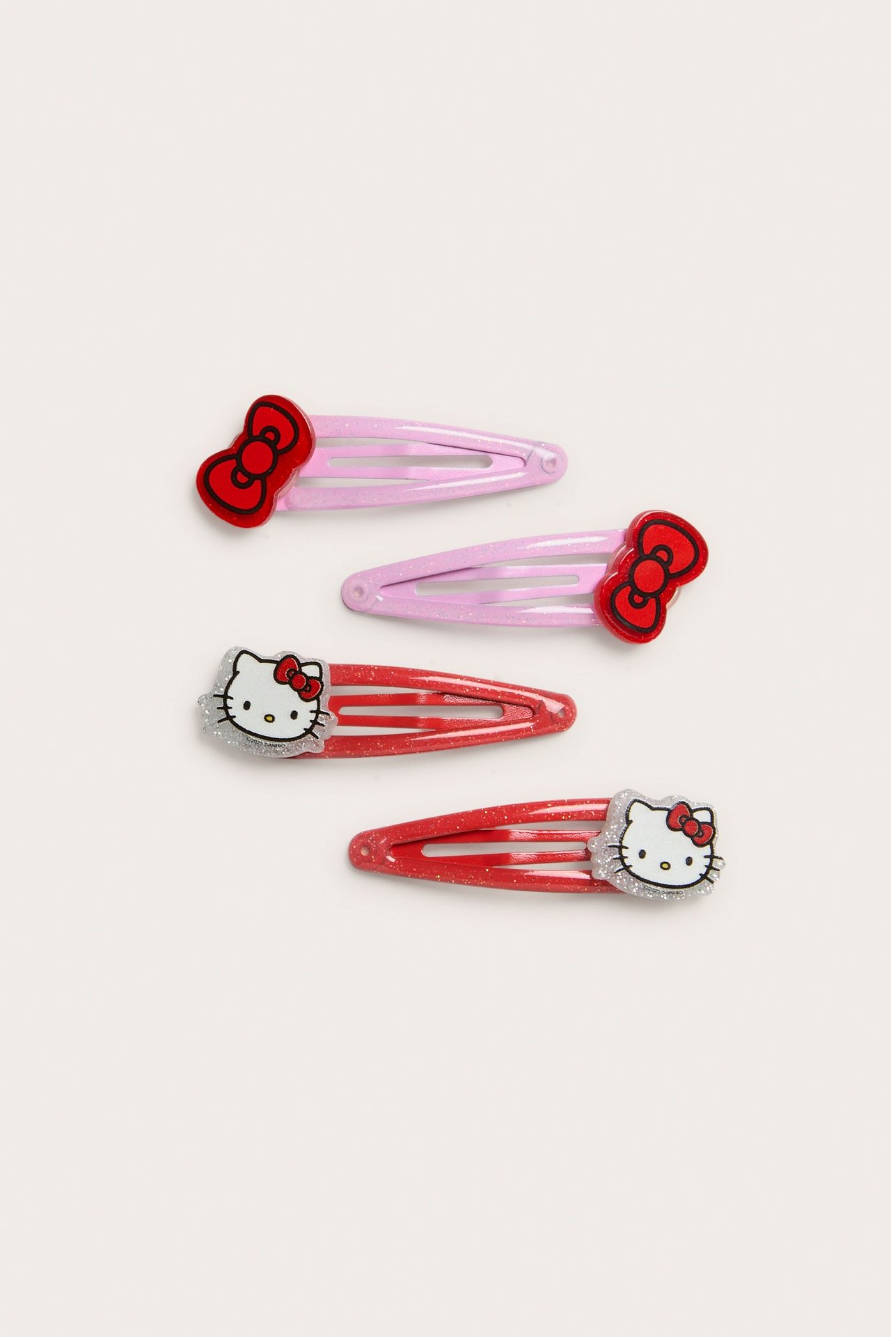Ylhäältä, neljä kimaltavaa Hello Kitty -hiusklipsiä: kaksi vaaleanpunaista, kaksi punaista kasvoilla.