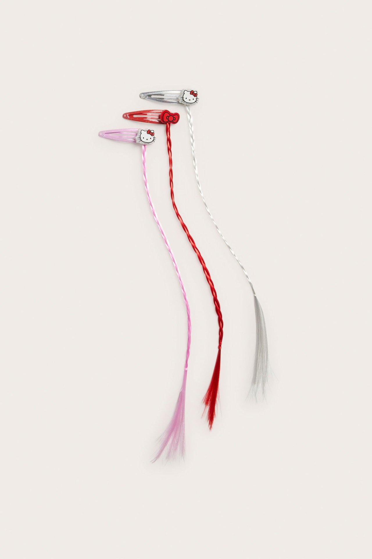 Lähikuva kolmesta lasten Hello Kitty -hiusklipsistä, joissa on vaaleanpunaiset, punaiset ja hopeiset letit.