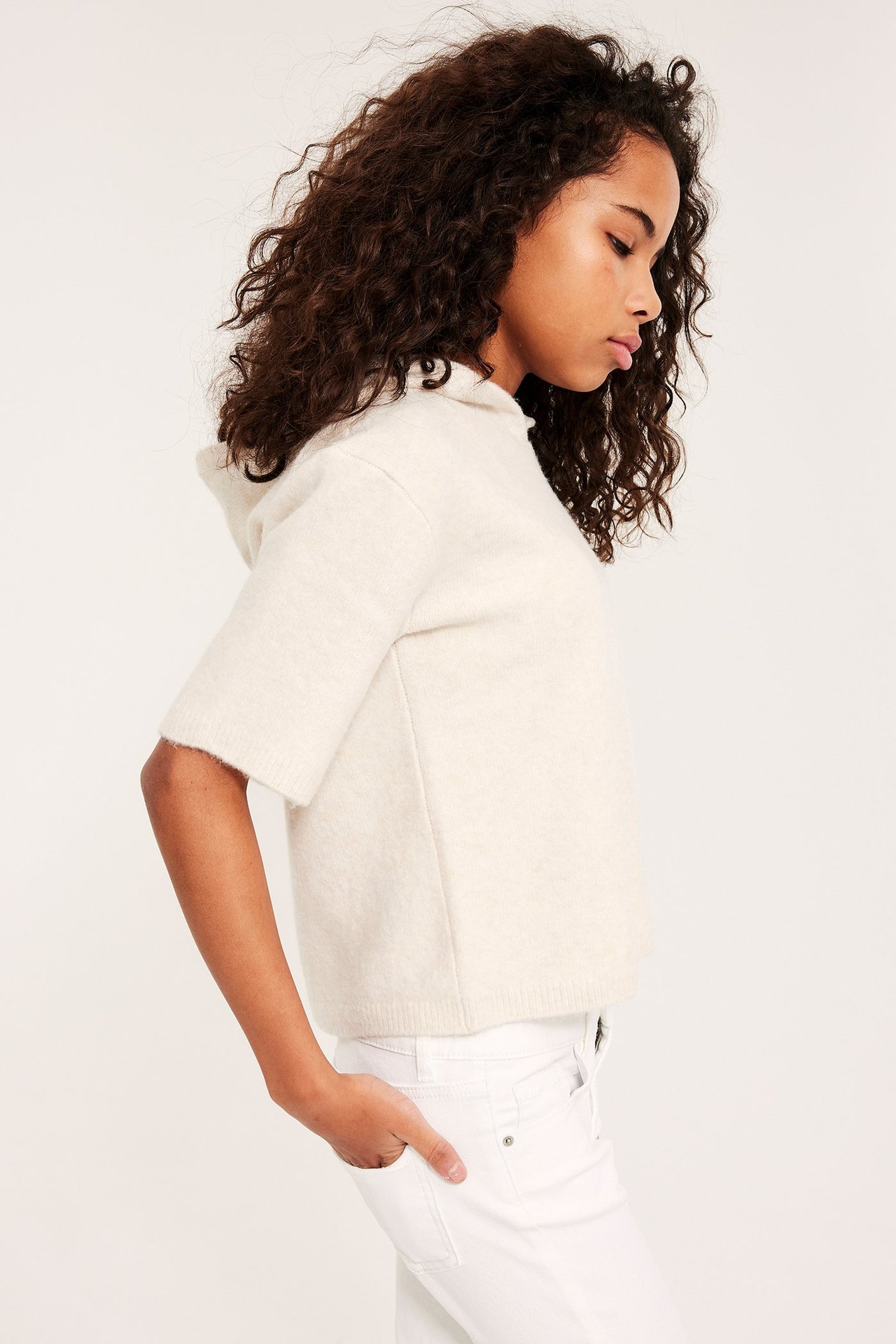 Sivukuva lapsesta yllään luonnonvalkoinen lyhythihainen neulepusero hupulla ja valkoiset housut.