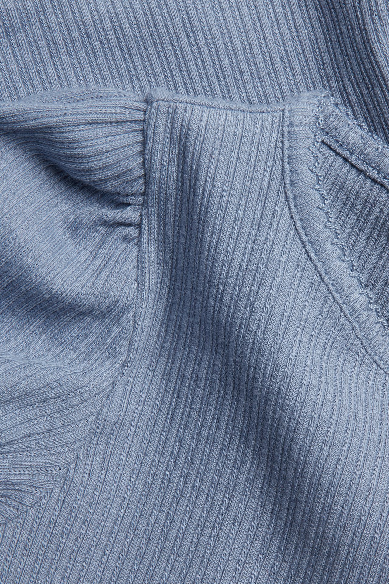 Zbliżenie na jasnoniebieski top z prążkowanej dzianiny z krótkimi bufiastymi rękawami i wykończeniem picot.