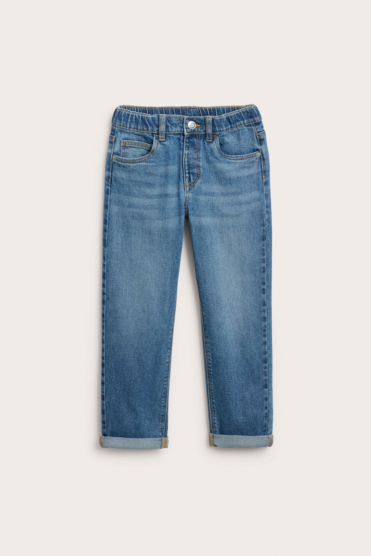 Forfra: Barnjeans i mellomblå farge med strikk i midjen, knapplukking og oppbrettede ankler.