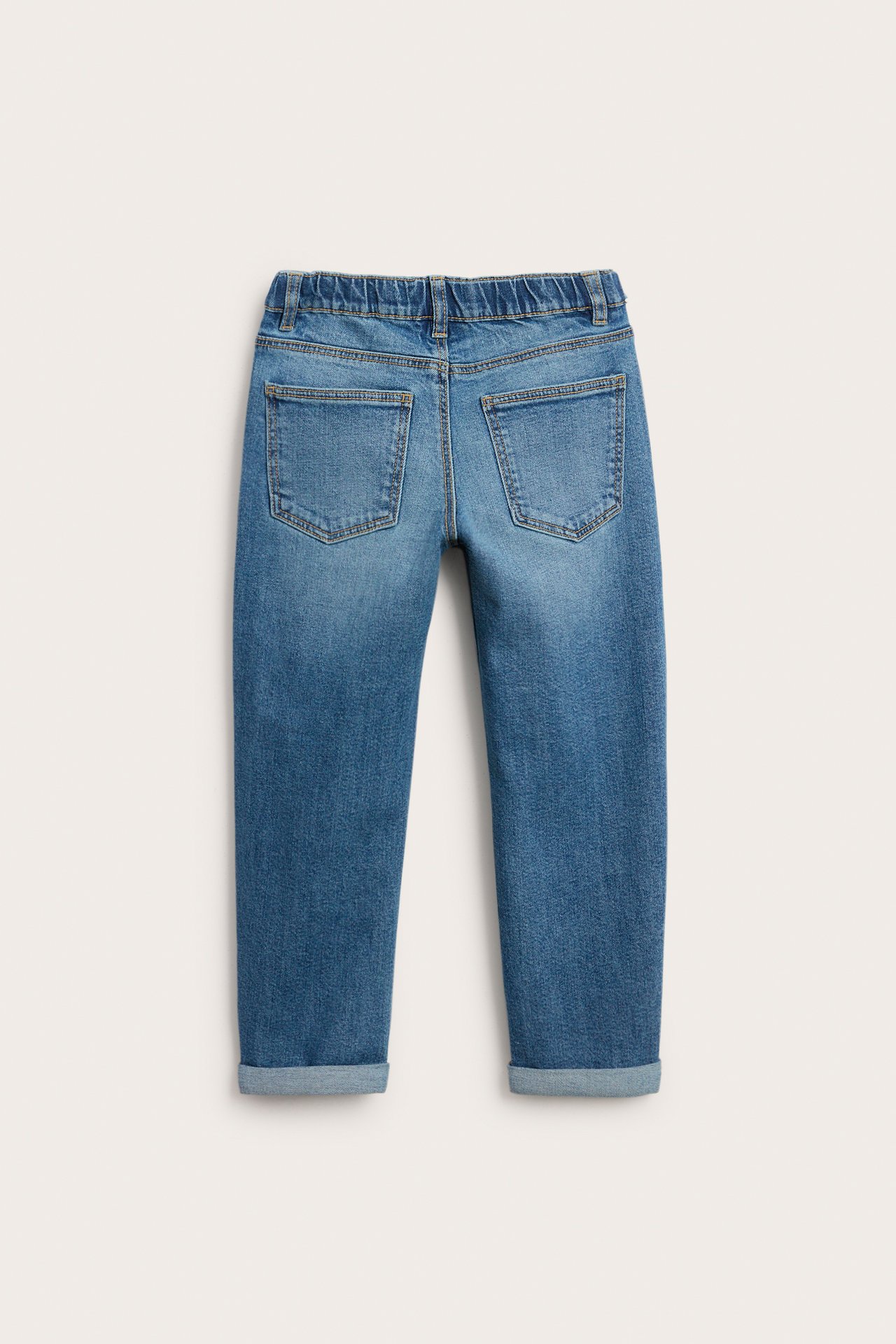 Bakfra av barnas blå denimjeans med elastisk linning og oppbrettede kanter.