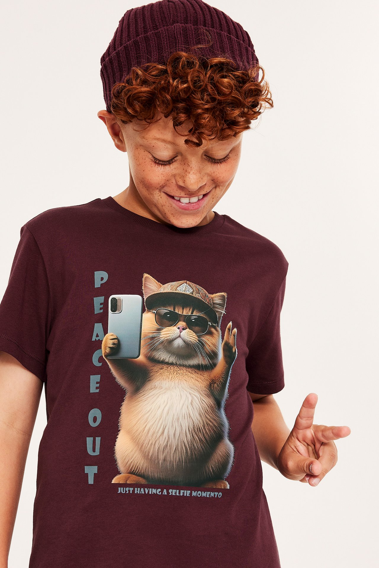 Chłopiec w ciemnoczerwonym T-shircie z nadrukiem psa, robi selfie.